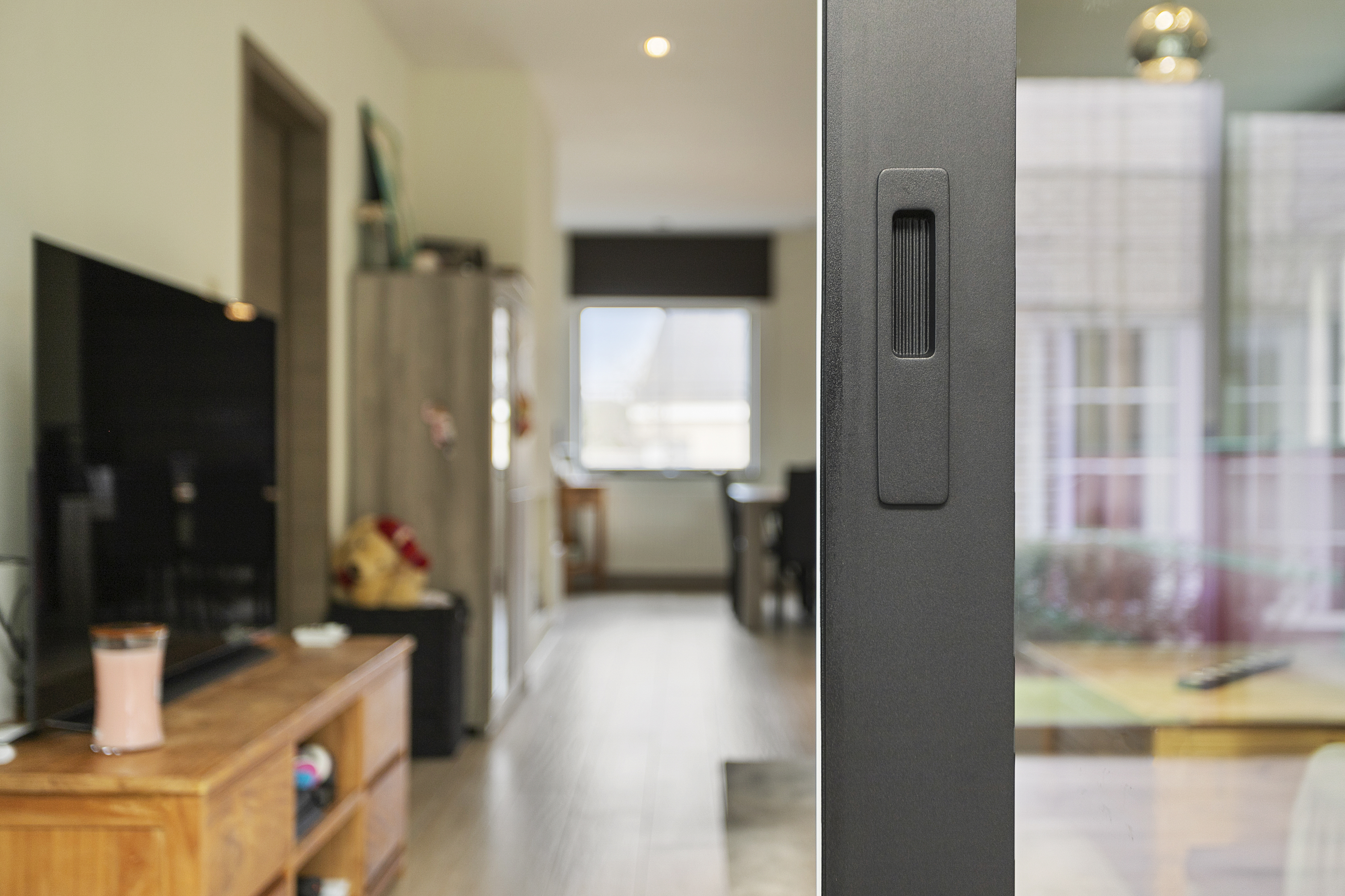 Close-up van een zwart aluminiumprofiel van een ALU Visoglide Monorail-schuifraam in een warm, landelijk interieur tijdens een renovatie.
