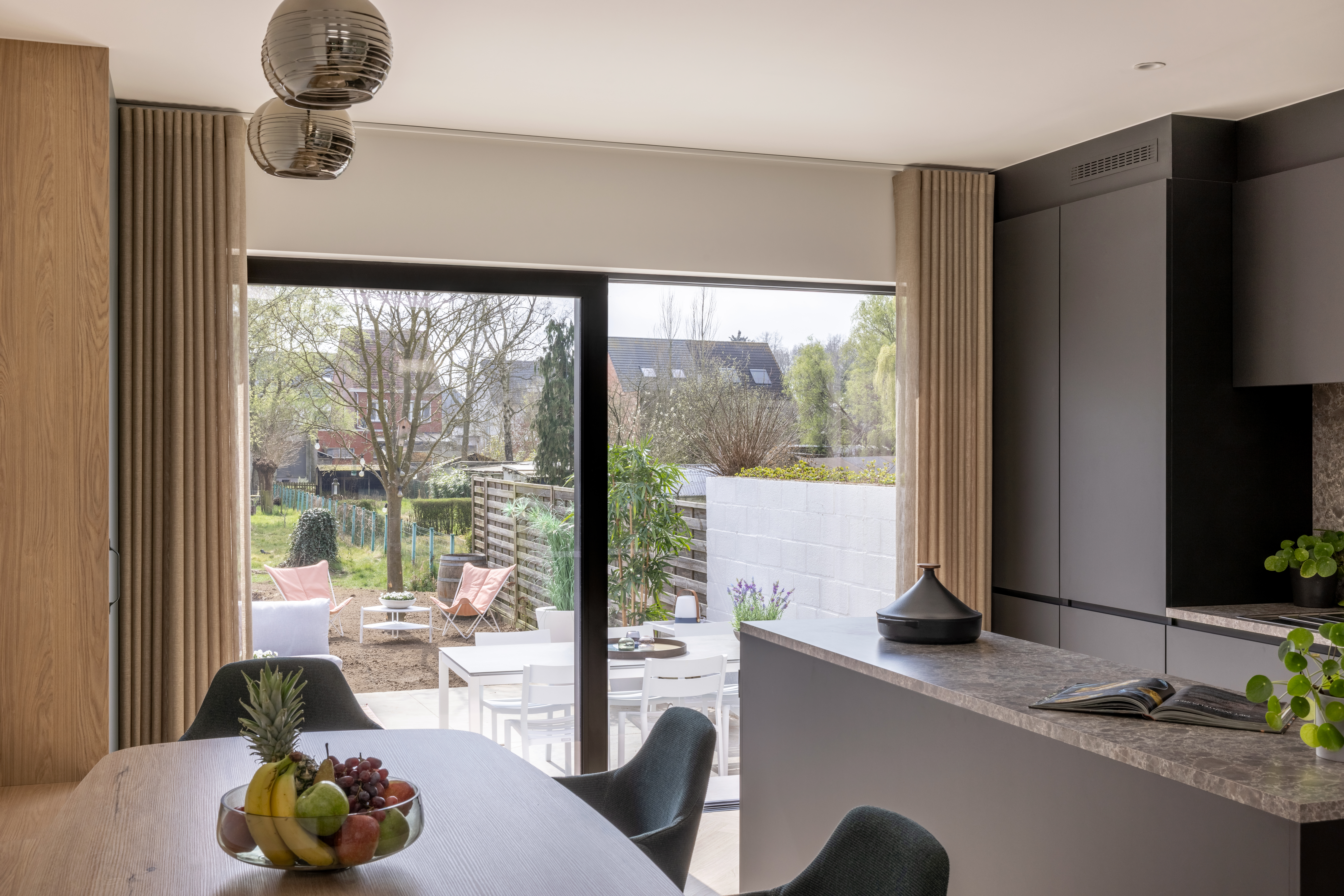 Moderne keuken met eethoek en groot schuifraam met uitzicht op het terras en de groene tuin.