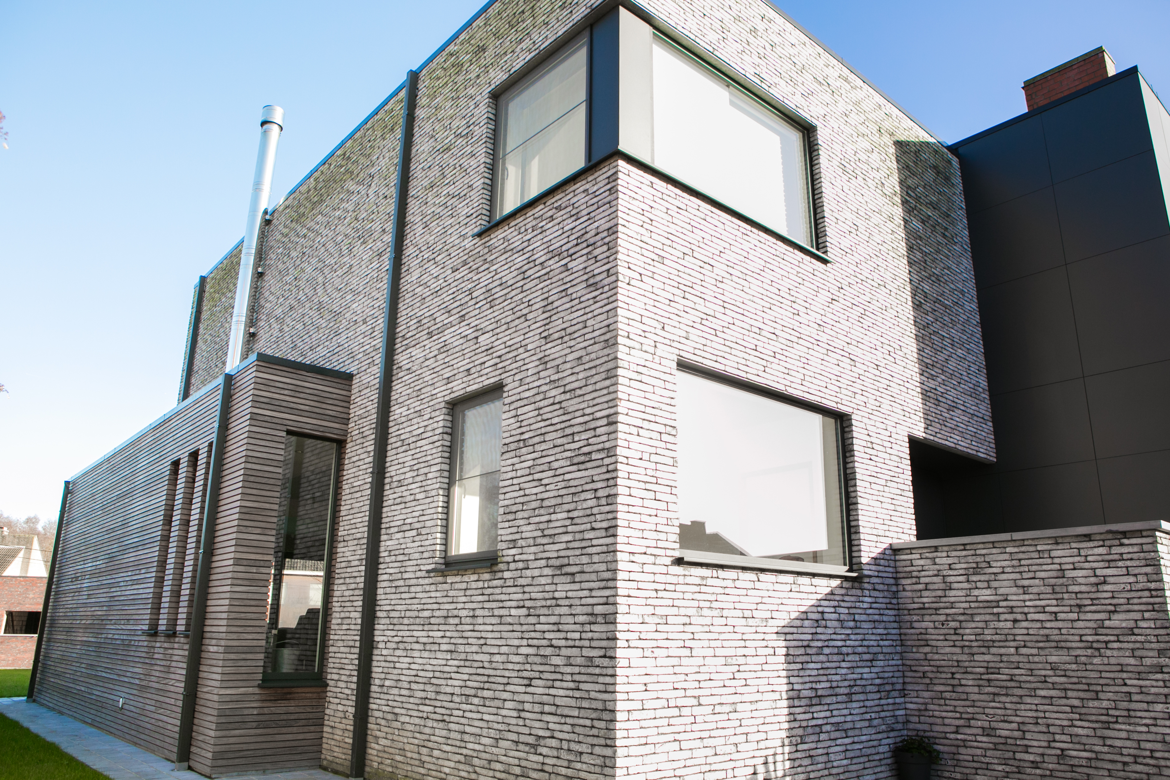 Moderne, vrijstaande nieuwbouwwoning met zwartgrijze raamprofielen, een hoekraam en grote vaste en draai-kiepramen in een bakstenen gevel.
