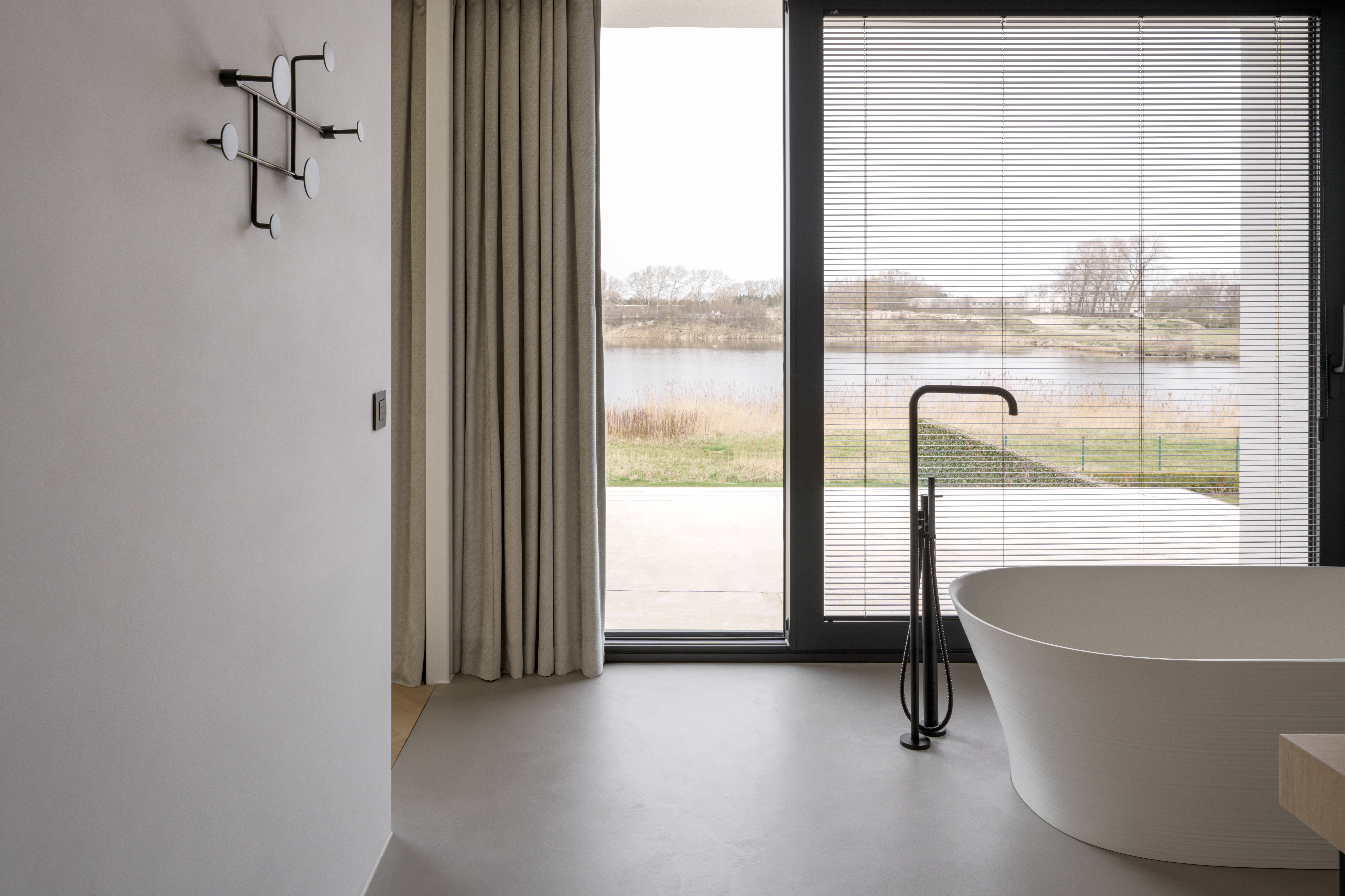 Moderne badkamer in een vrijstaande nieuwbouwwoning met zwart ALU Ultraglide Monorail-schuifraam, ligbad en uitzicht op het water.