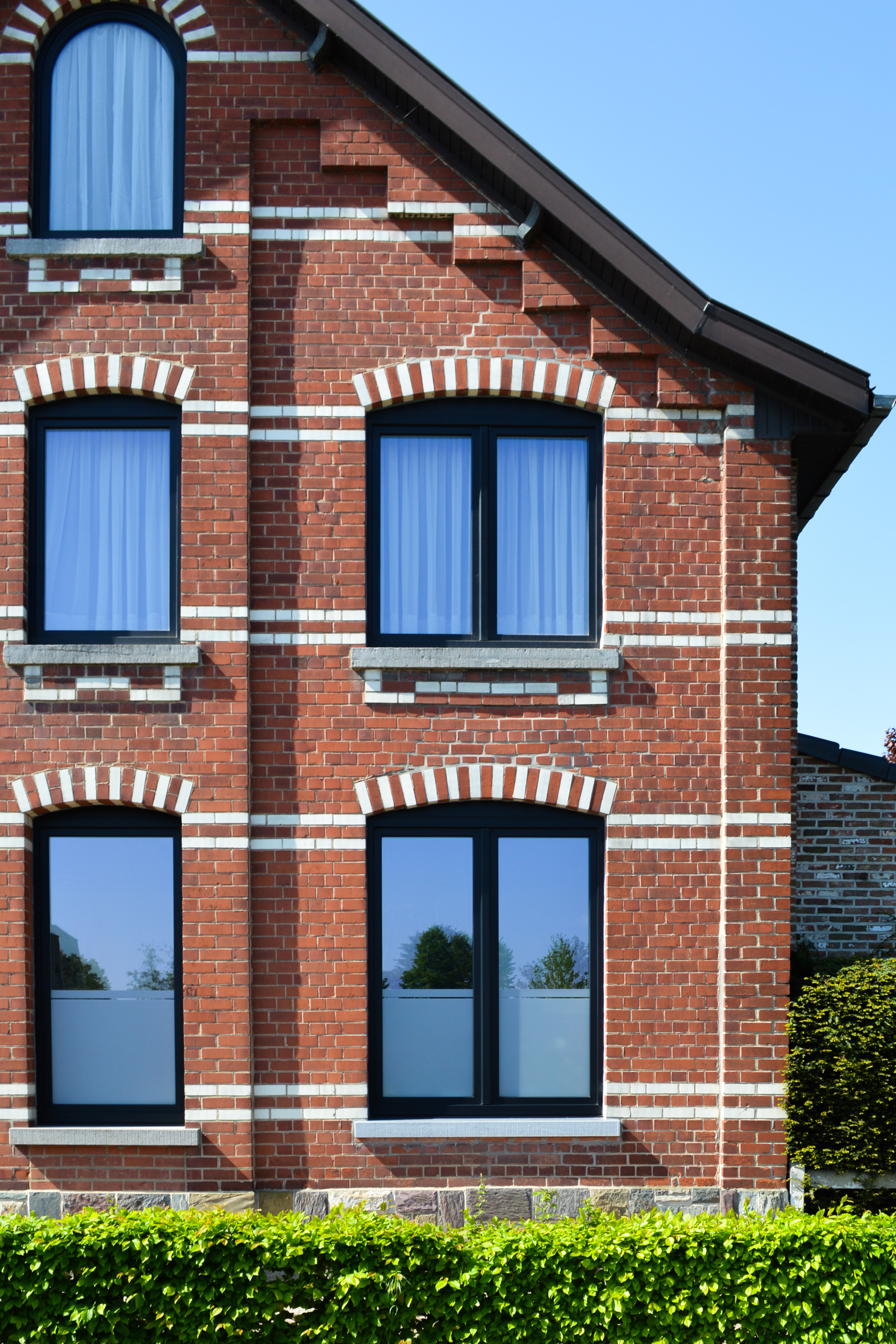 Rode bakstenen gevel met zwarte matte raamprofielen, waaronder een dubbel raam en een draai-kipraam, afgewerkt met witte bakstenen accenten.