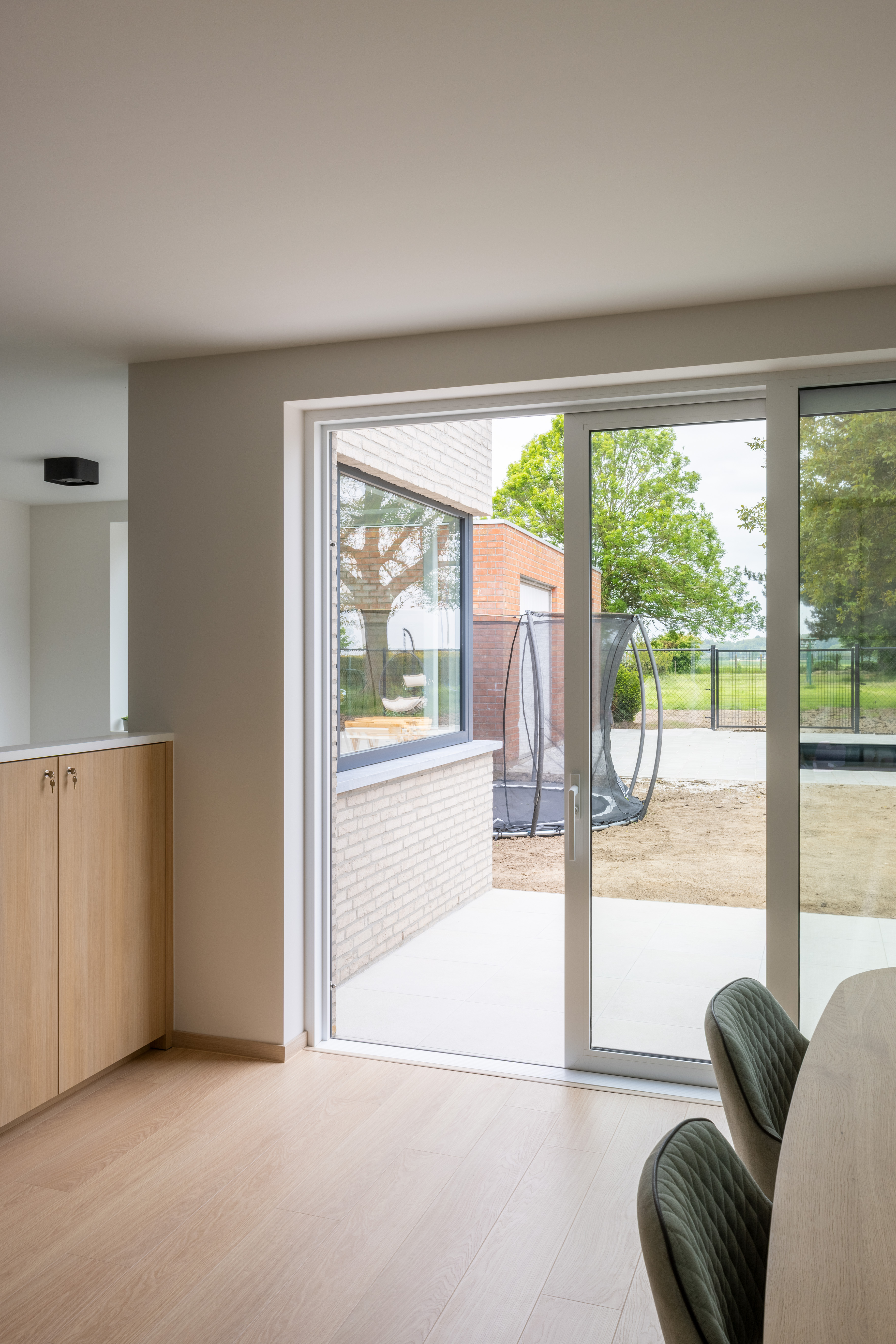 Modern aluminium schuifraam in mat verkeerswit met schuifvliegenraam, in een gerenoveerd interieur met zicht op een afgesloten buitenruimte.