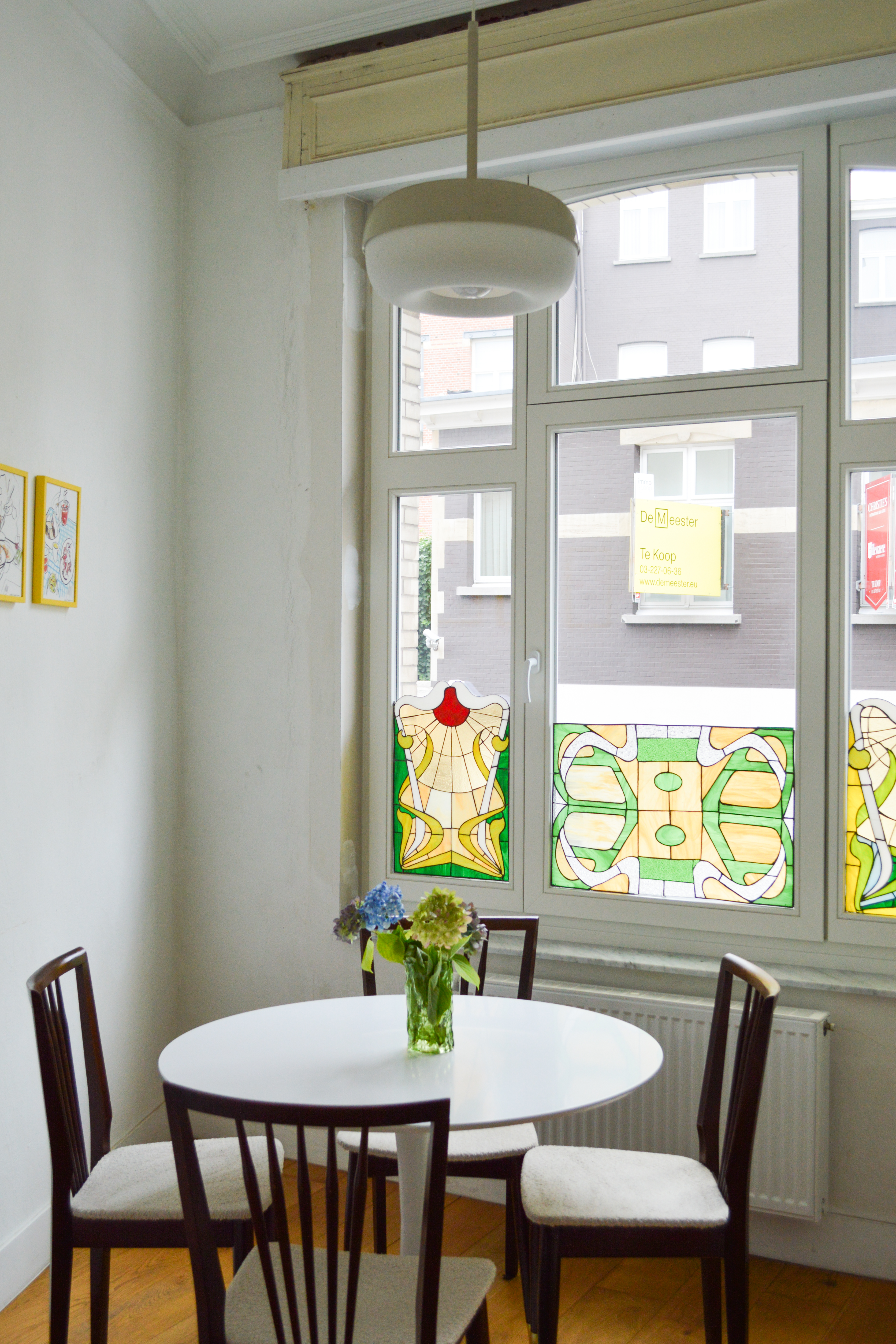 Verfijnd klassiek interieur met wit afgelakte ramen: een vast raam, draai-kipraam en bovenlicht boven een eettafel in gesloten bebouwing.