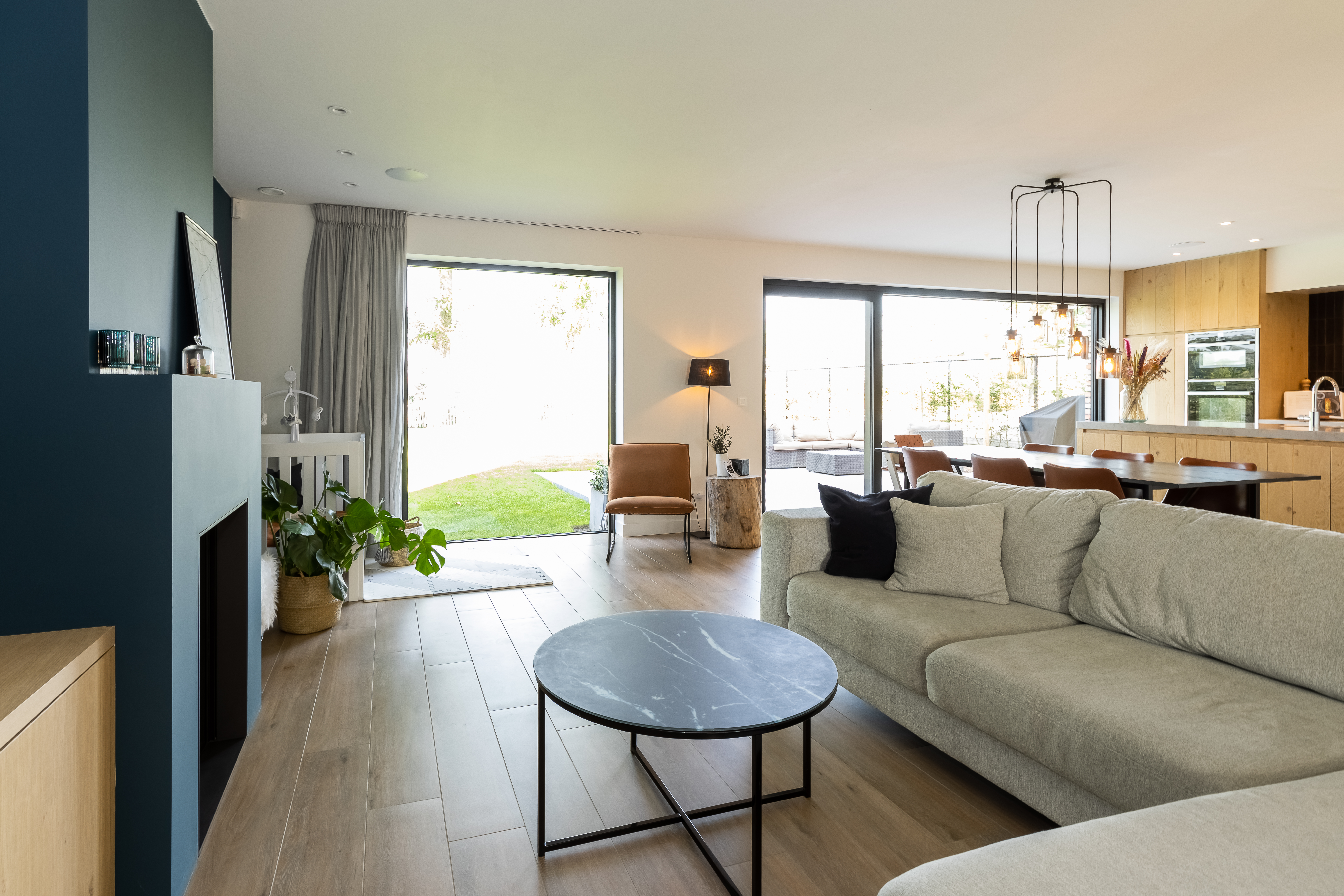 Lichte leefruimte in warme landelijke stijl met een vast, diepzwart aluminiumraam, grote beglazing en zicht op de tuin in een nieuwbouwwoning.
