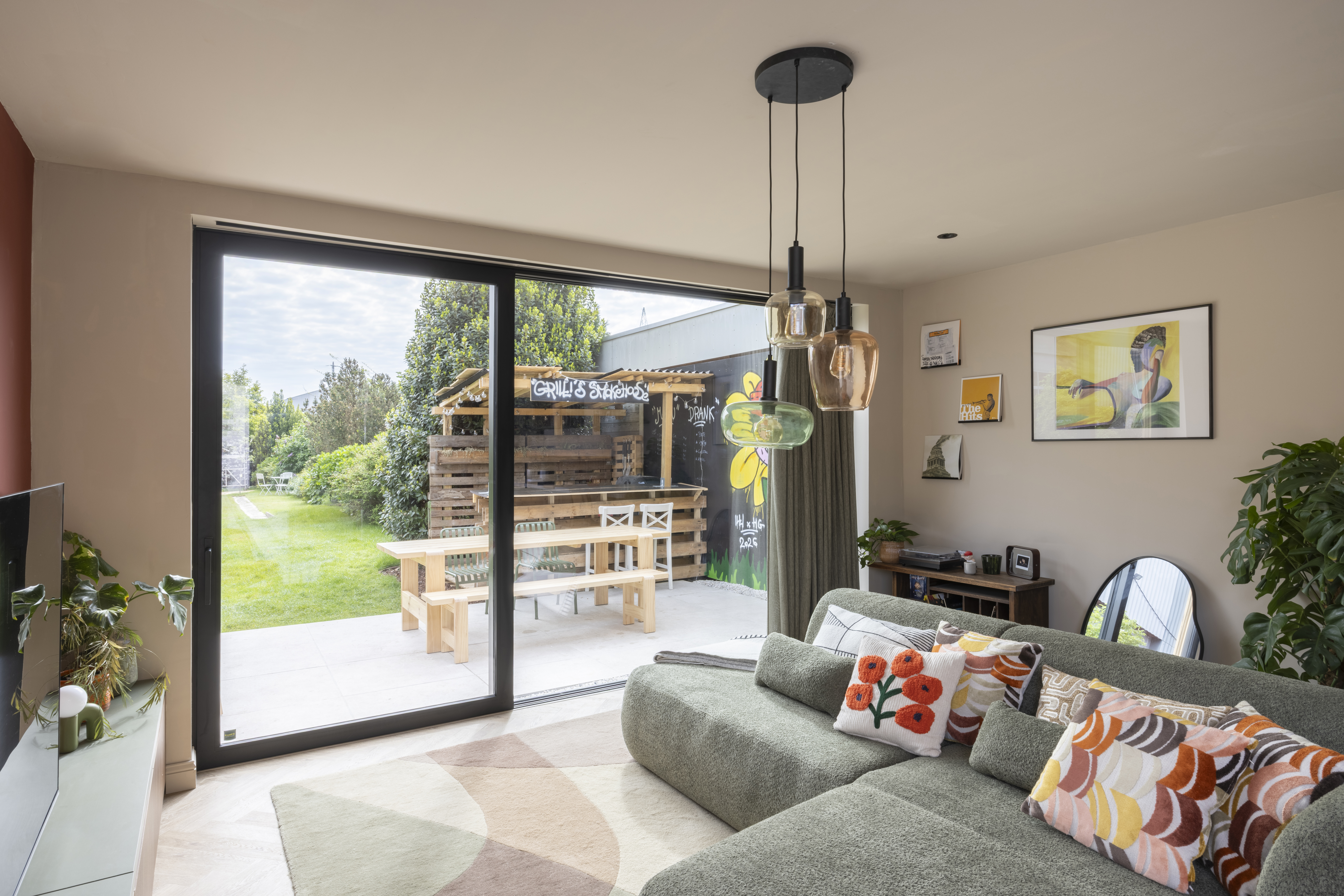Groot diepzwart ALU Visoglide Monorail-schuifraam in de woonkamer, met uitzicht op de tuin en de overdekte zithoek.