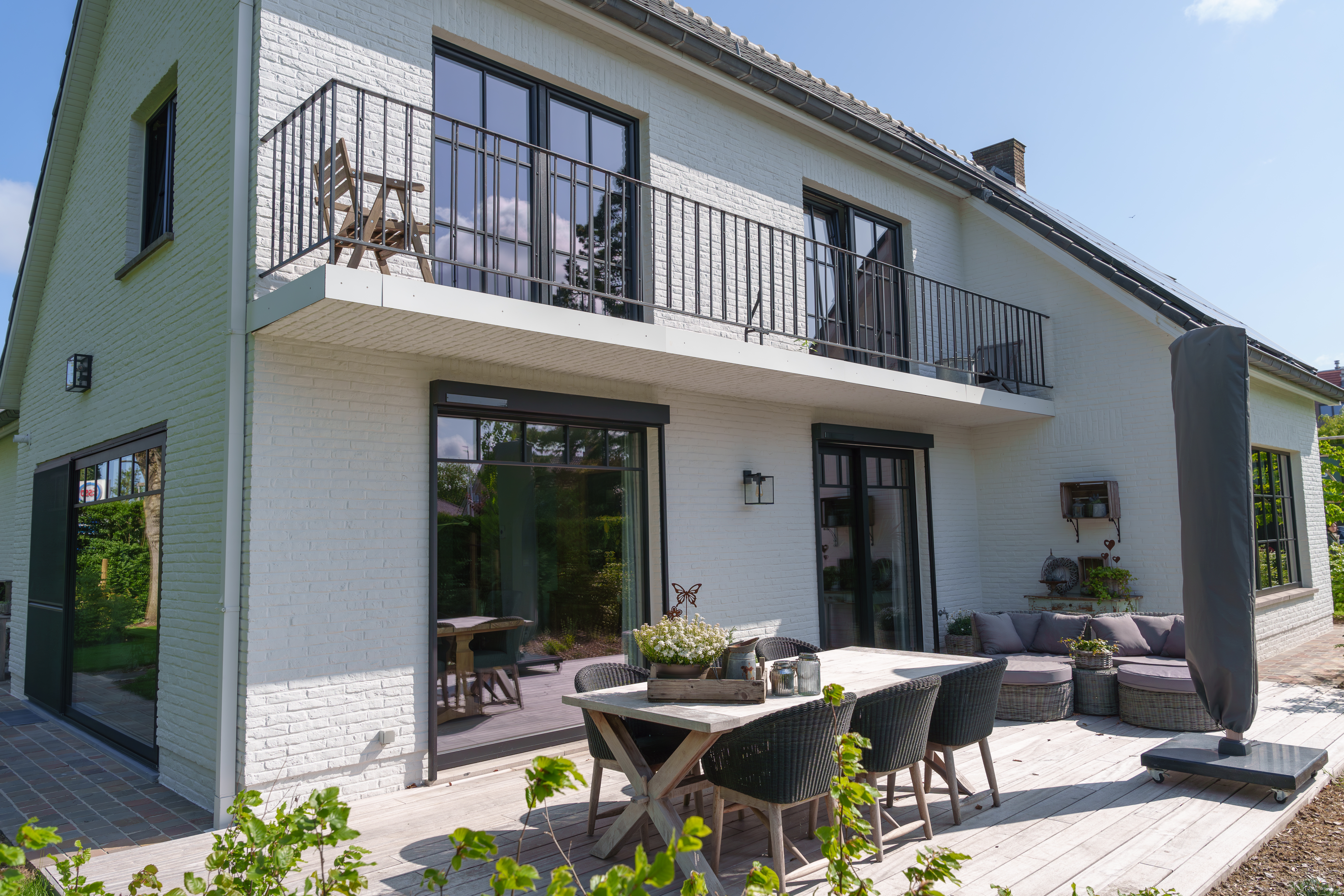 Witte woning met matzwarte raamprofielen, een vast raam en een dubbel raam, een balkon met balustrade en een voorzetrolluik aan het terras.