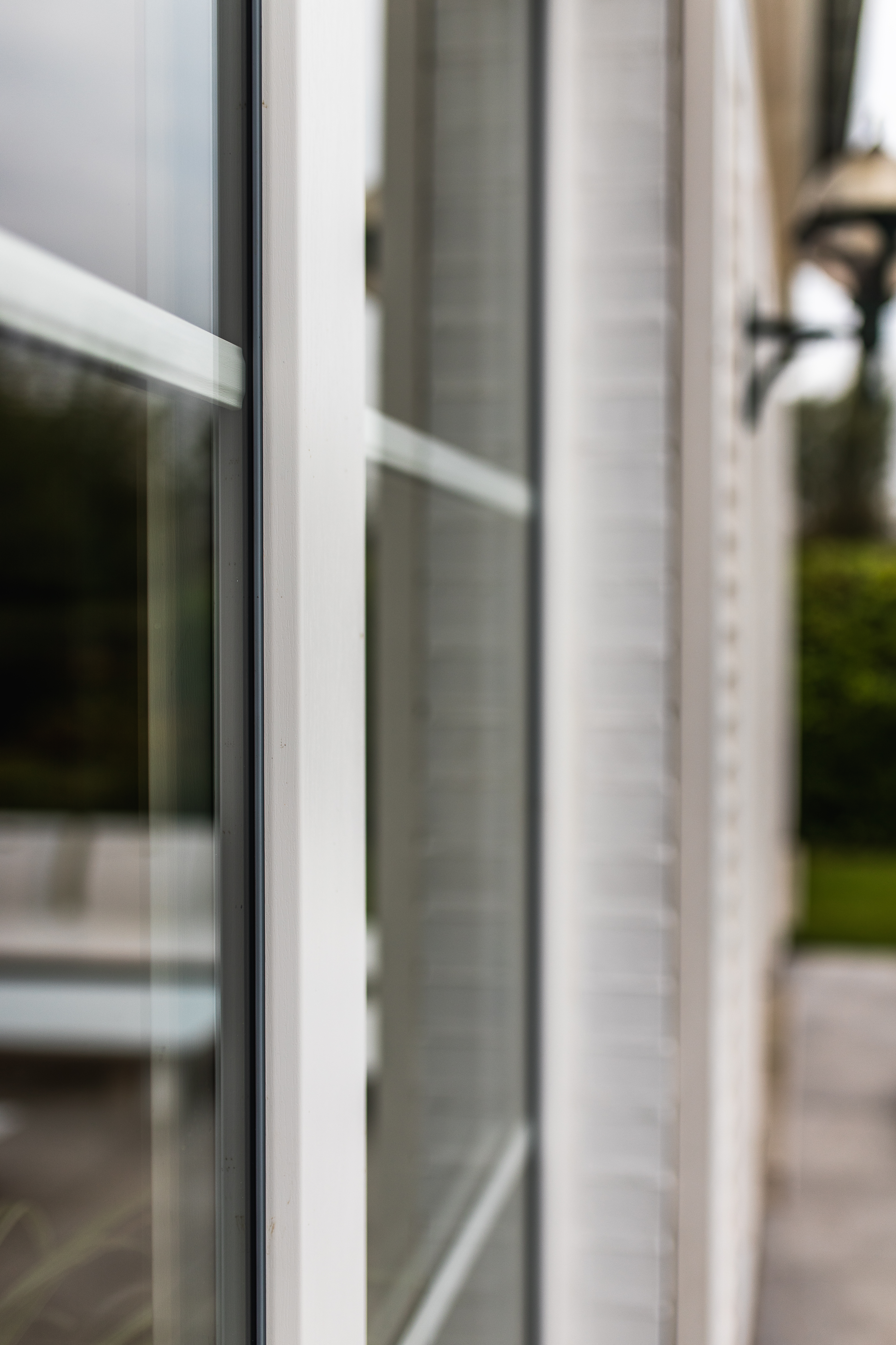 Detail van verfijnde klassieke witte raamprofielen tussen glas, passend bij een renovatie van een open bebouwing met zicht op de tuin.