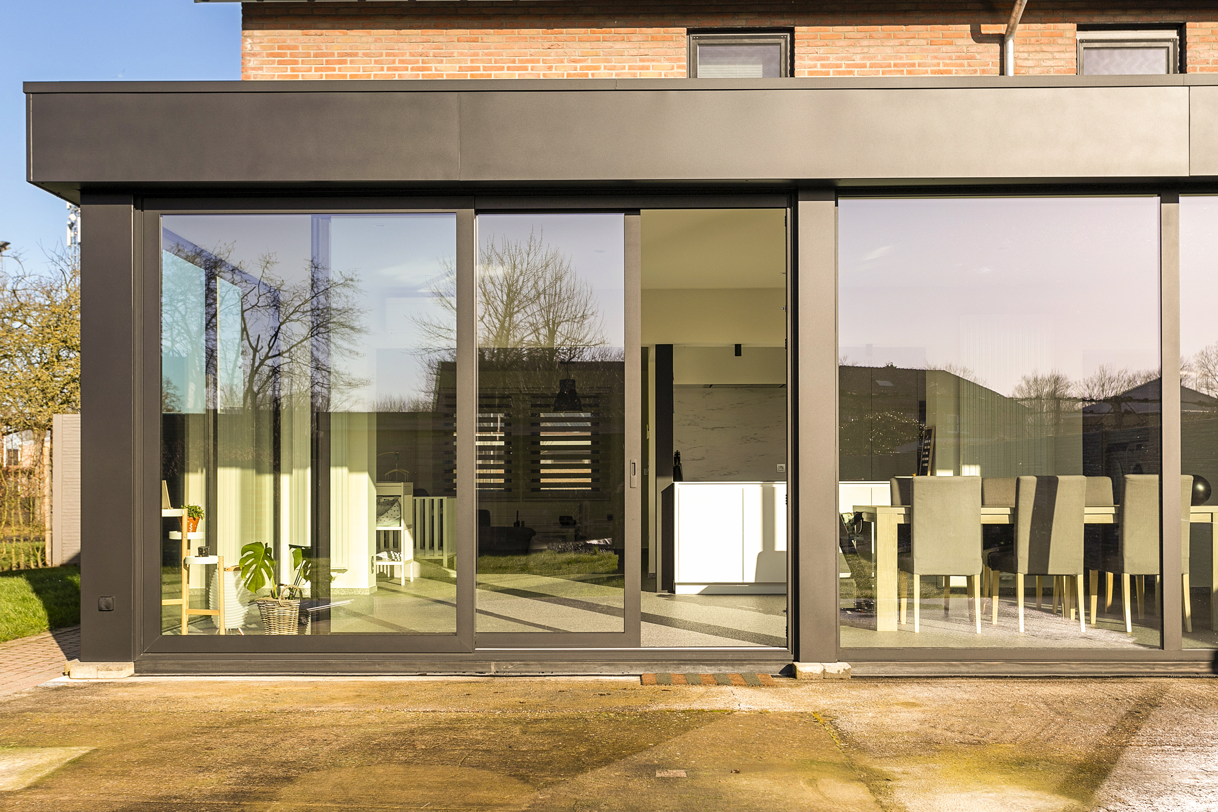 Groot vast aluminiumraam in signaalzwart aan een gerenoveerde woninggevel, met donkere raamprofielen en zicht op het lichte interieur.