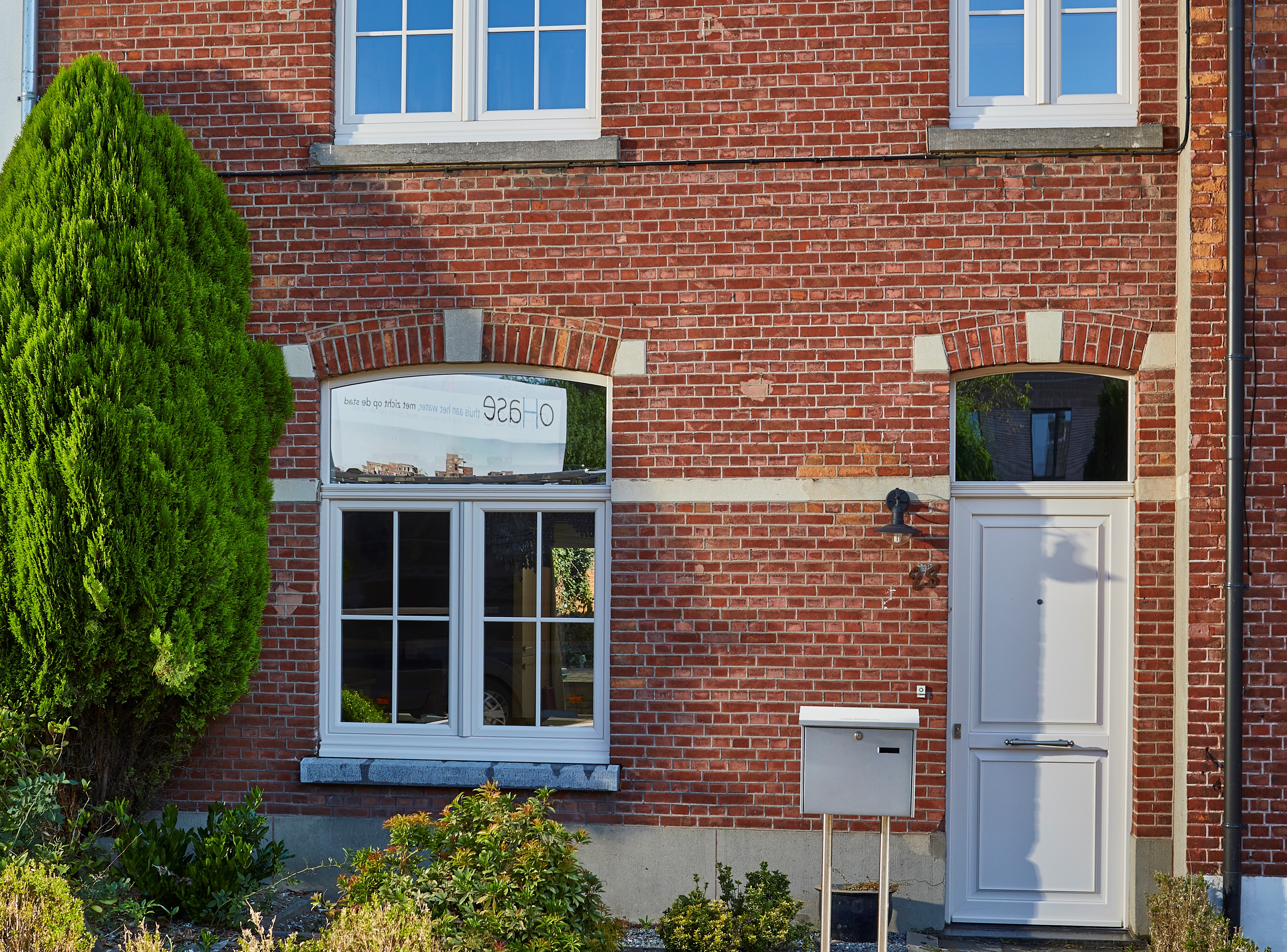 Gerestaureerde gevel in rode baksteen met een verfijnde klassieke crèmekleurige paneeldeur met bovenlicht en een bijpassend raam.