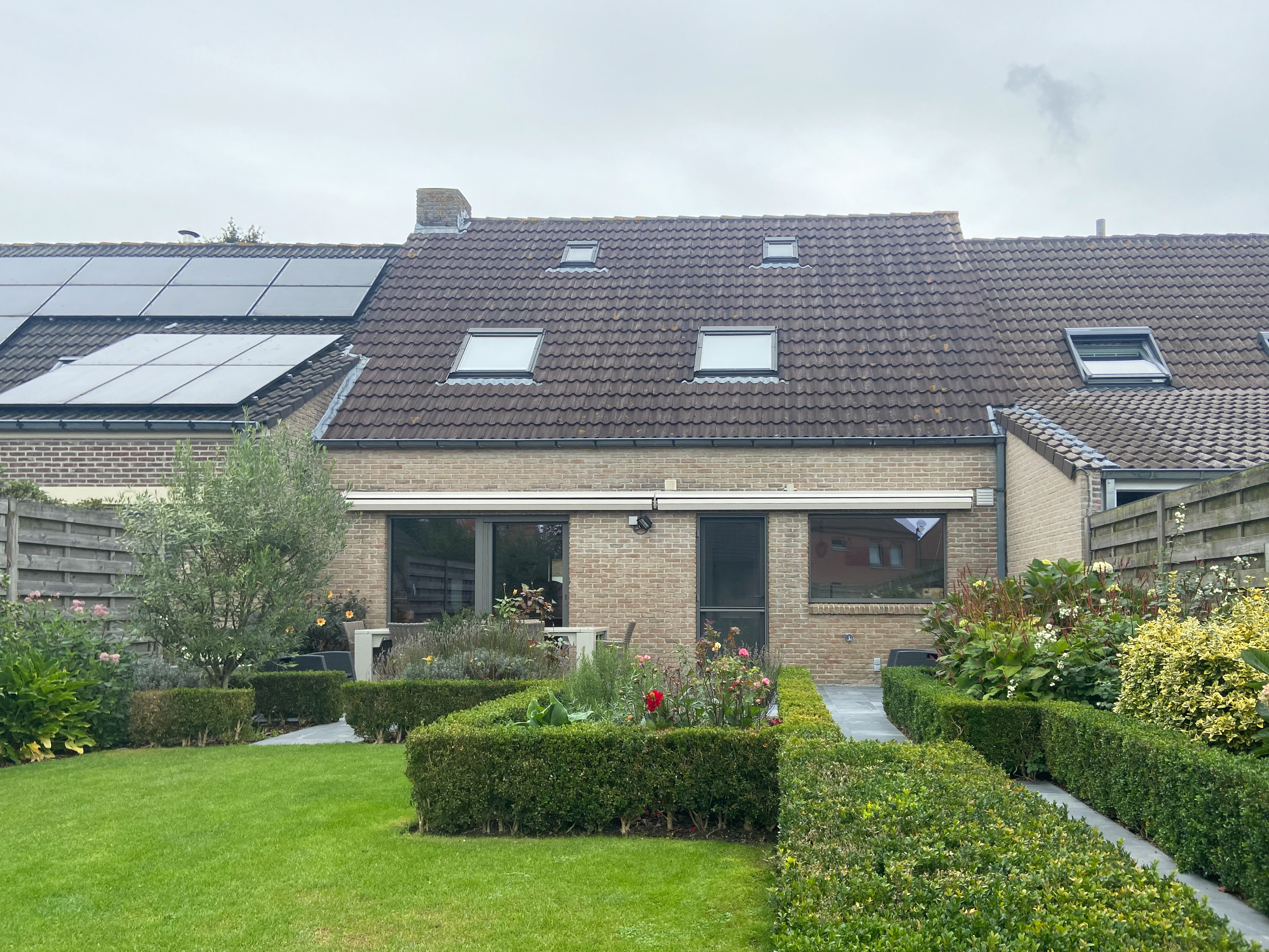 Gemoedelijke, tijdloze achtergevel van een gerenoveerde open bebouwing met grote ramen, een verzorgde tuin en een hellend pannendak.