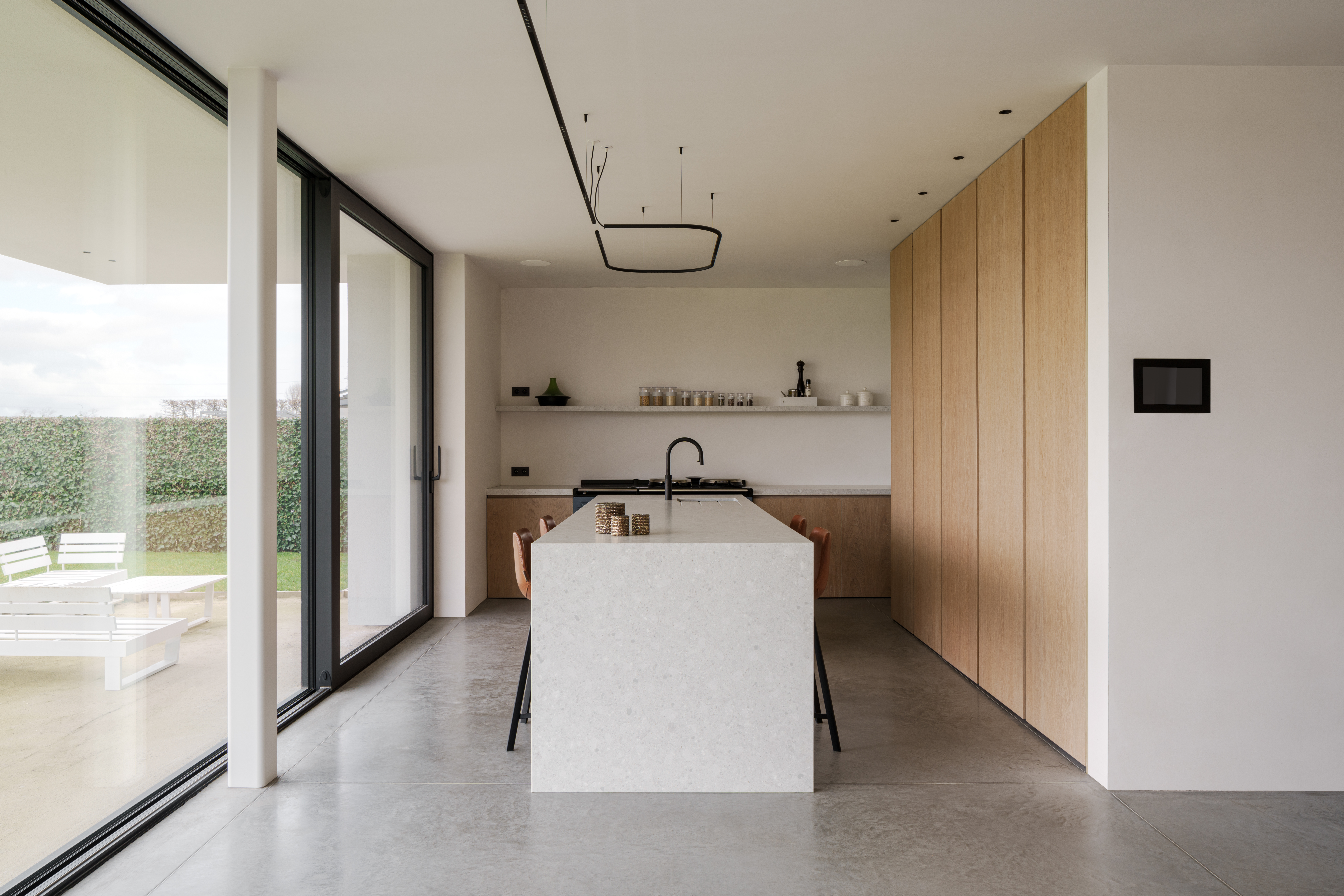 Moderne nieuwbouwwoning met een zwart ALU Ultraglide Monorail-schuifraam, een lichte keuken met kookeiland, houten fronten en zicht op het terras.