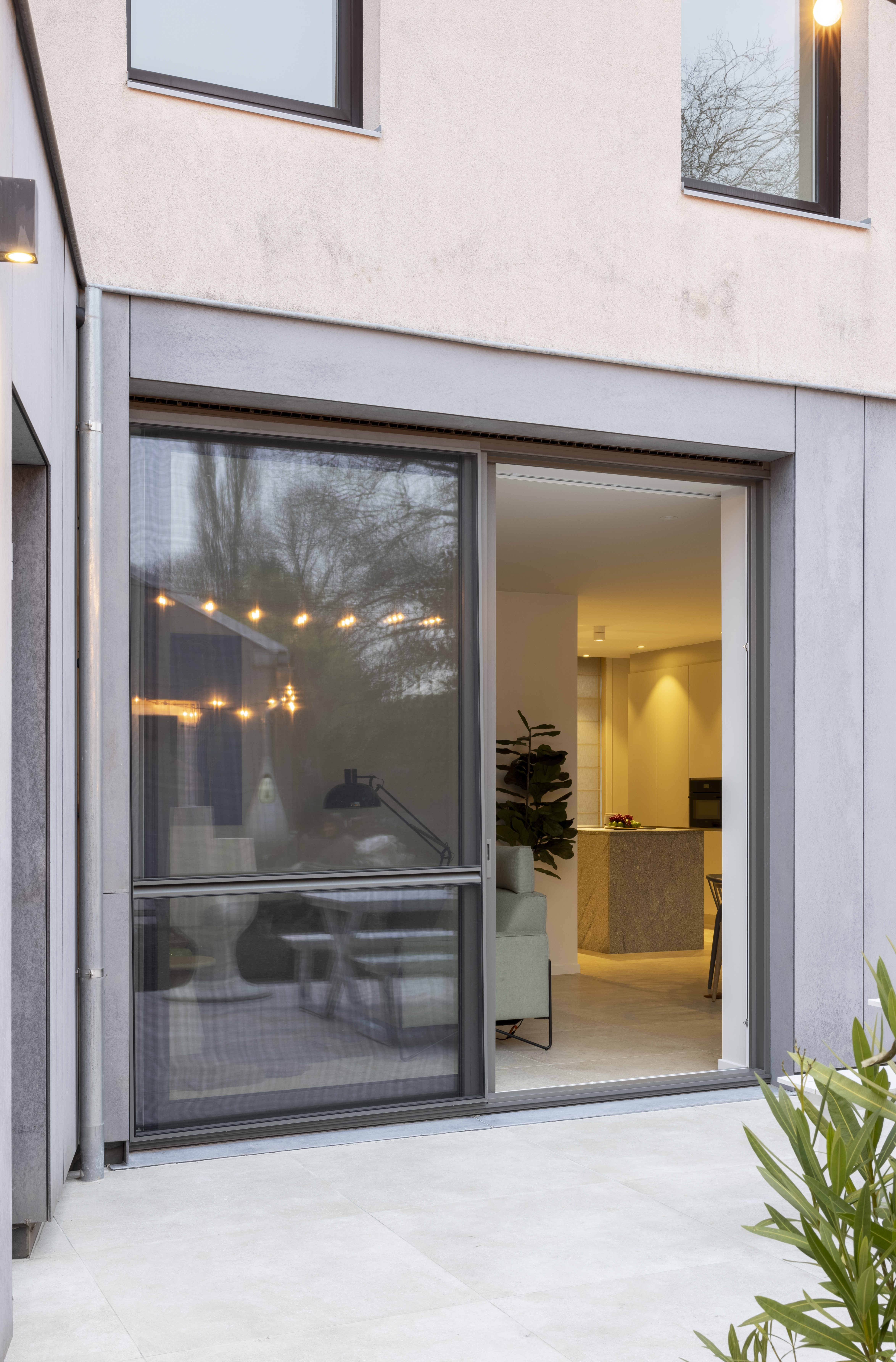 Moderne gesloten bebouwing met een kwartsgrijs ALU Visoglide Monorail-schuifraam en schuifvliegenraam in het kader van een renovatie.