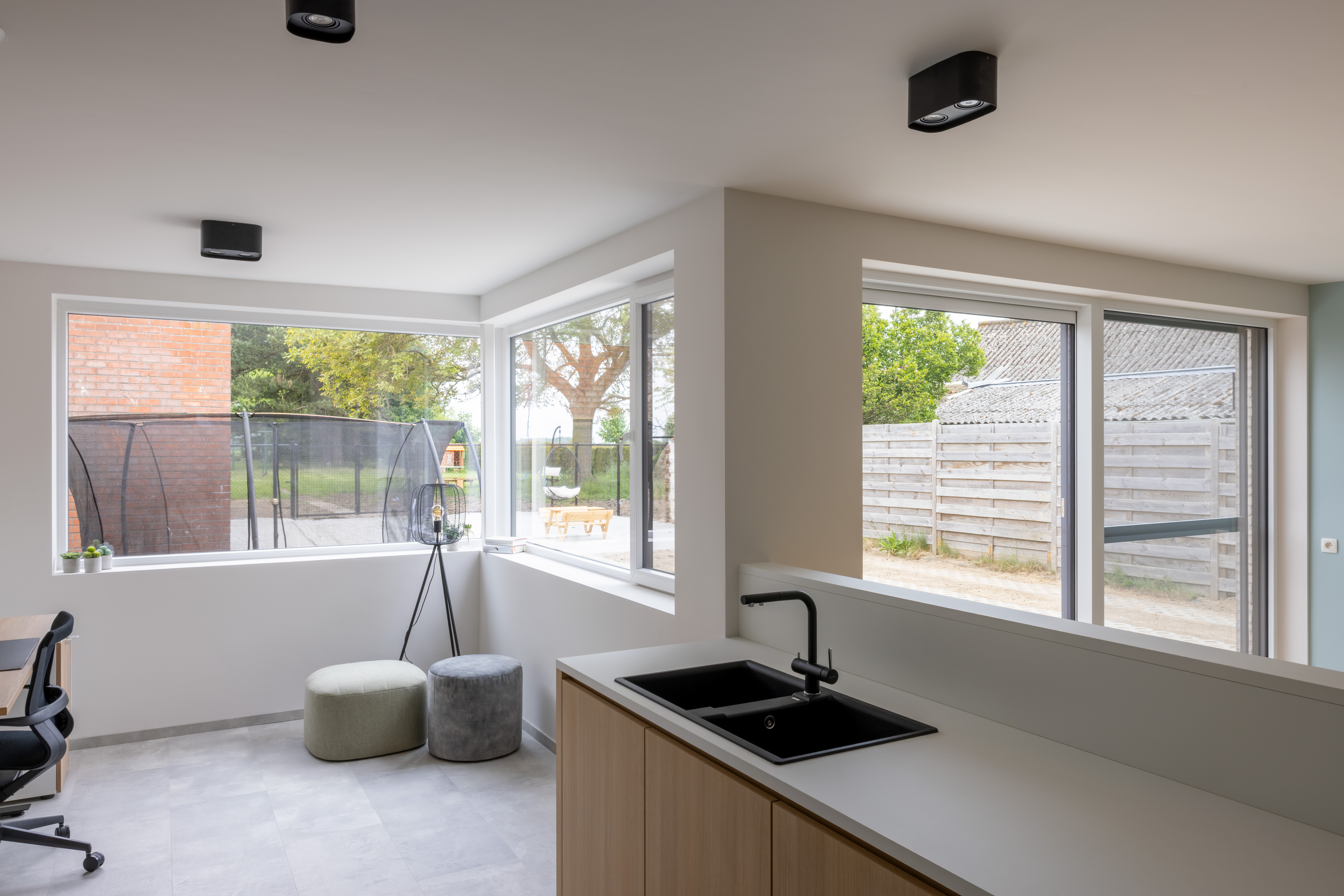 Lichte, moderne keuken met witte aluminium raamprofielen, een vast raam en een draai-kipraam met schuifvliegenraam en uitzicht op de tuin.