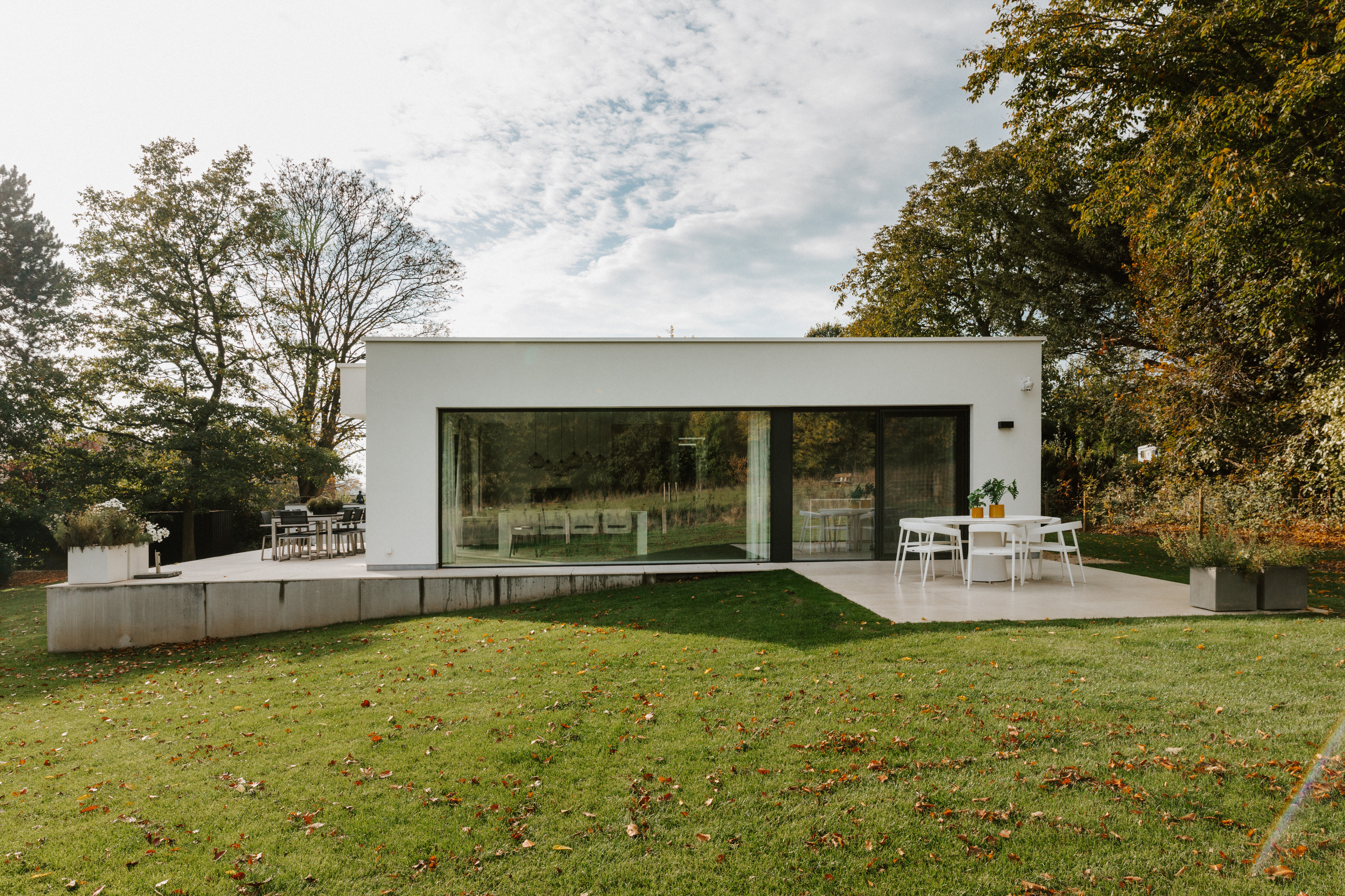 Moderne vrijstaande woning met een groot vast raam in zwarte aluminiumprofielen en een schuifvliegenraam, aan de tuinzijde met terras en gazon.