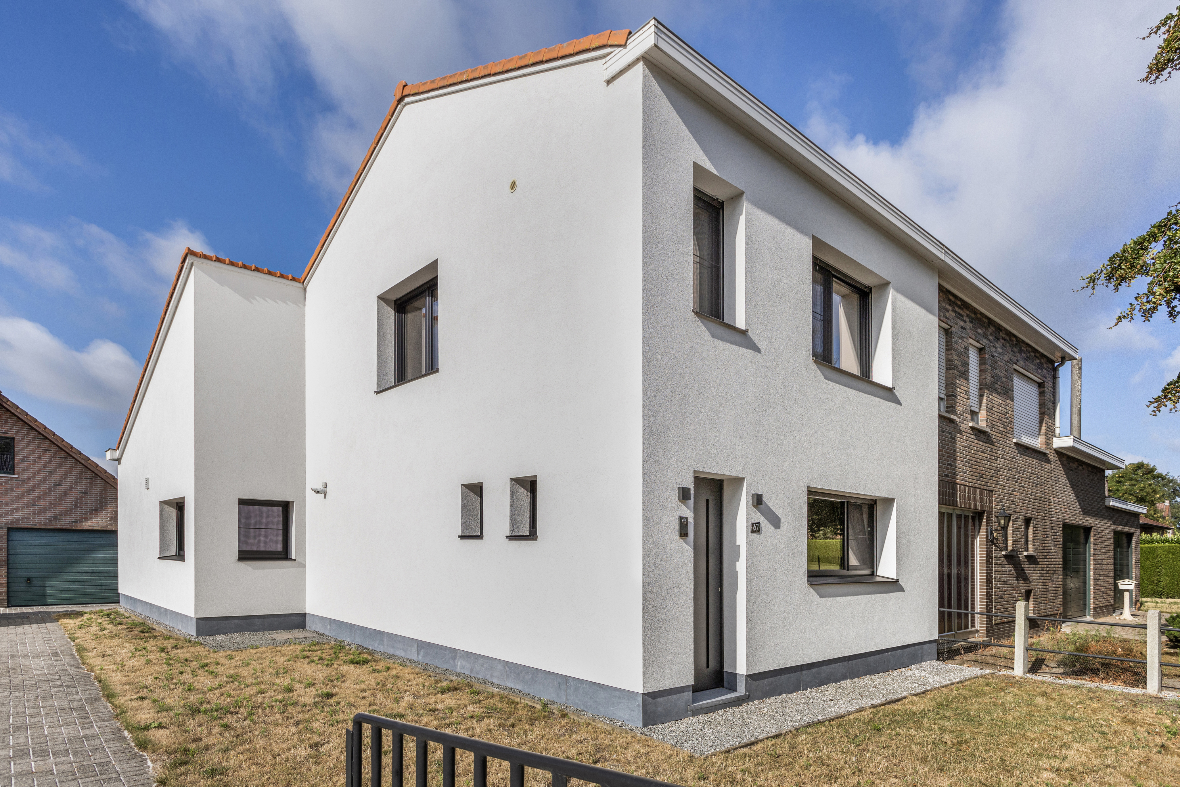 Moderne halfopen woning met witte gevel, matzwarte pvc-ramen en een combinatie van dubbele ramen en draai-kipramen.