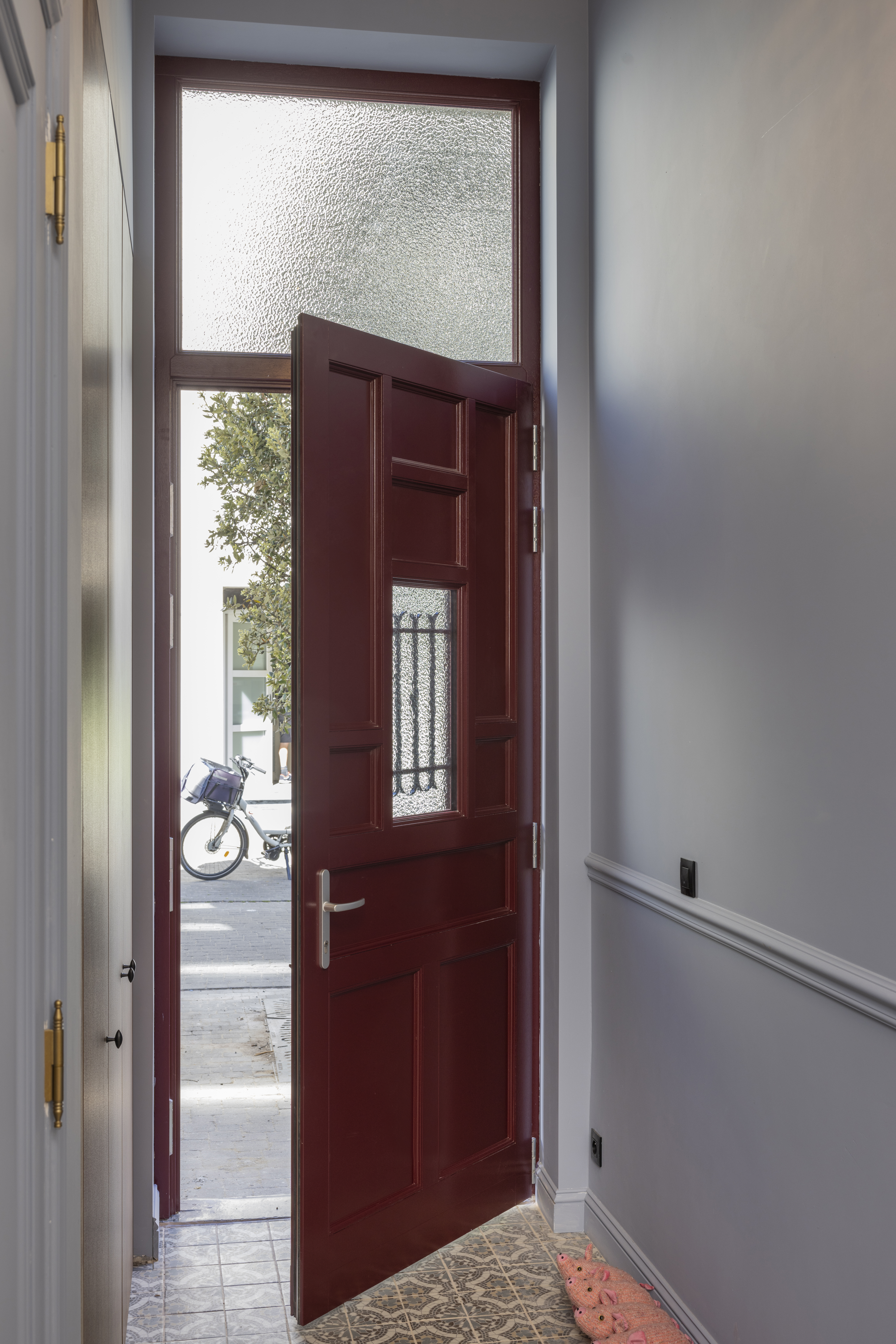 Wijnrode Meranti-voordeur met bovenlicht, naar binnen geopend; door de beglazing zijn de straat en een fiets zichtbaar.