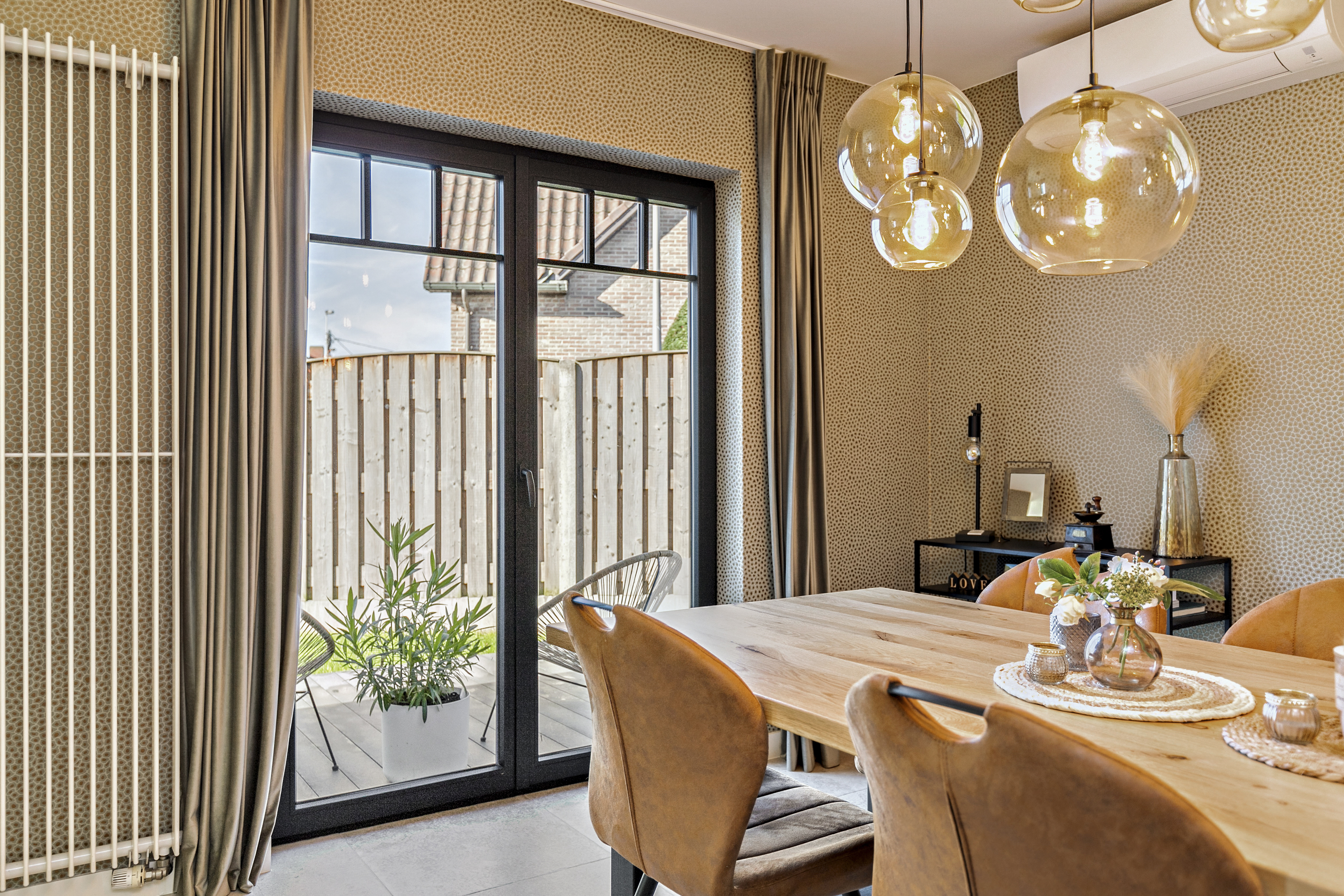 Matzwart draai-kipraam en dubbel raam in een eetruimte met houten tafel en gestoffeerde stoelen, met zicht op een omheinde buitenruimte.