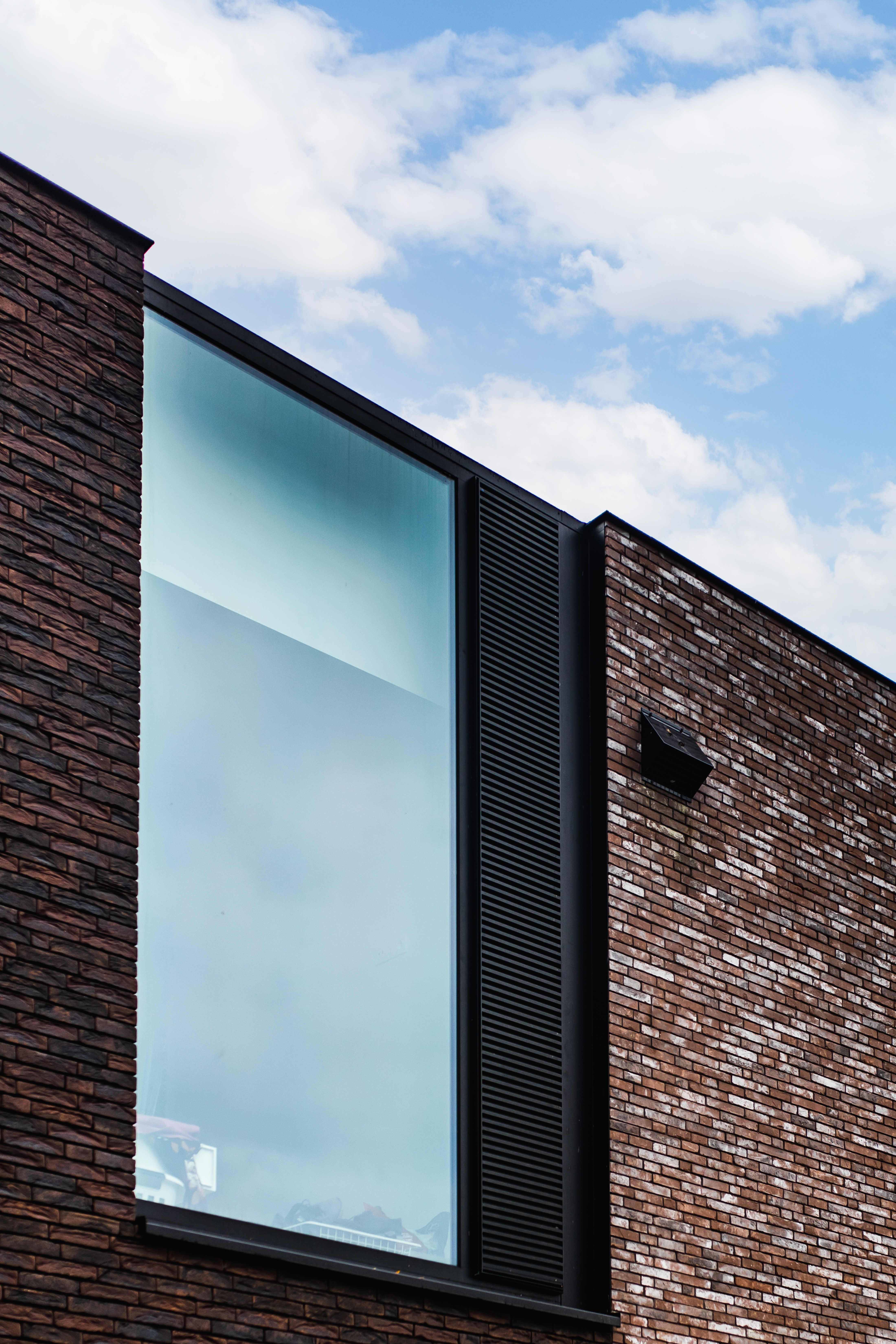 Moderne bakstenen gevel van een nieuwbouwwoning met een groot verticaal raam en zwarte raamprofielen bij een vrijstaande woning.