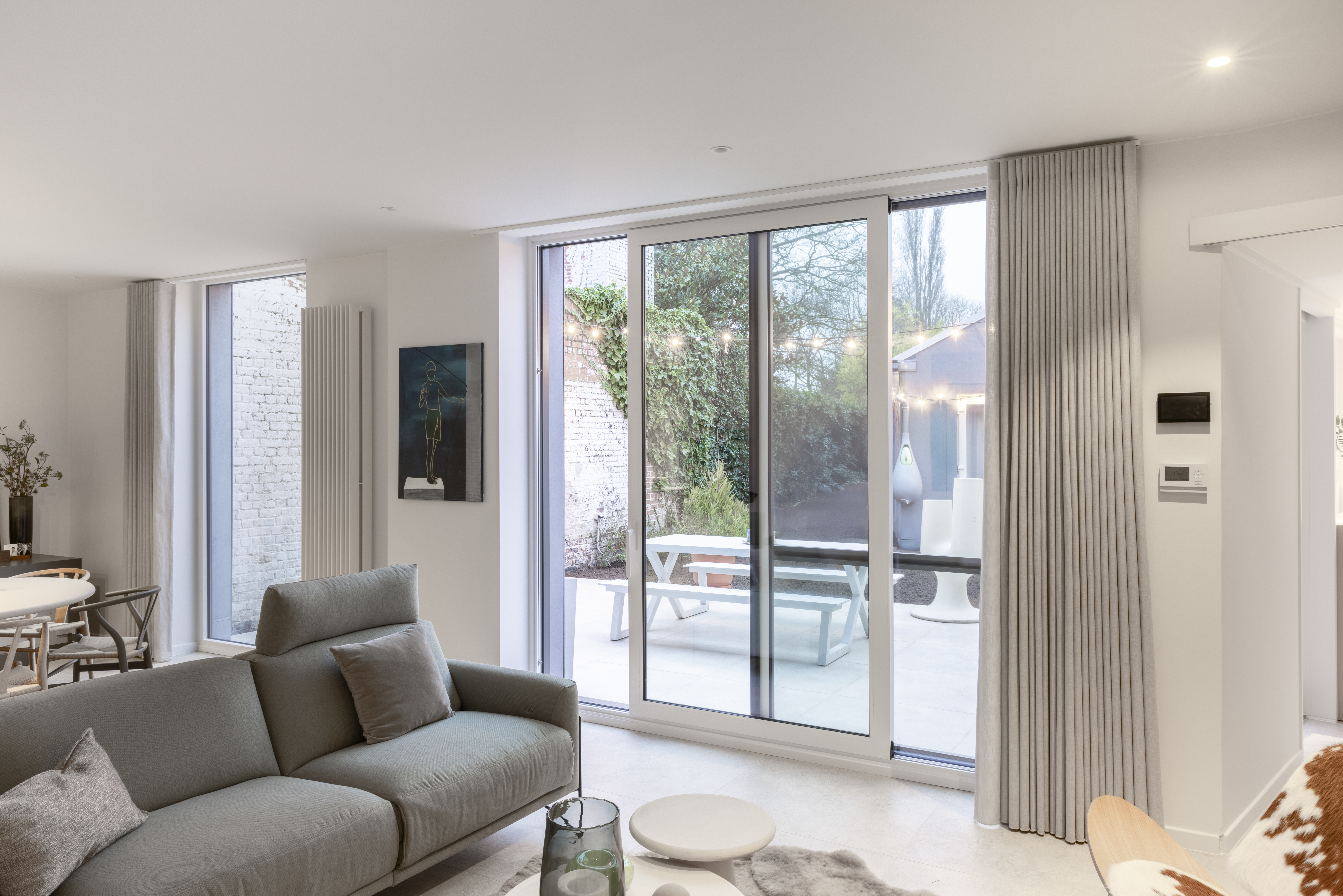 Modern vast raam in wit aluminium in een gerenoveerde woning, met grote glaspartijen die de woonkamer verbinden met het terras.