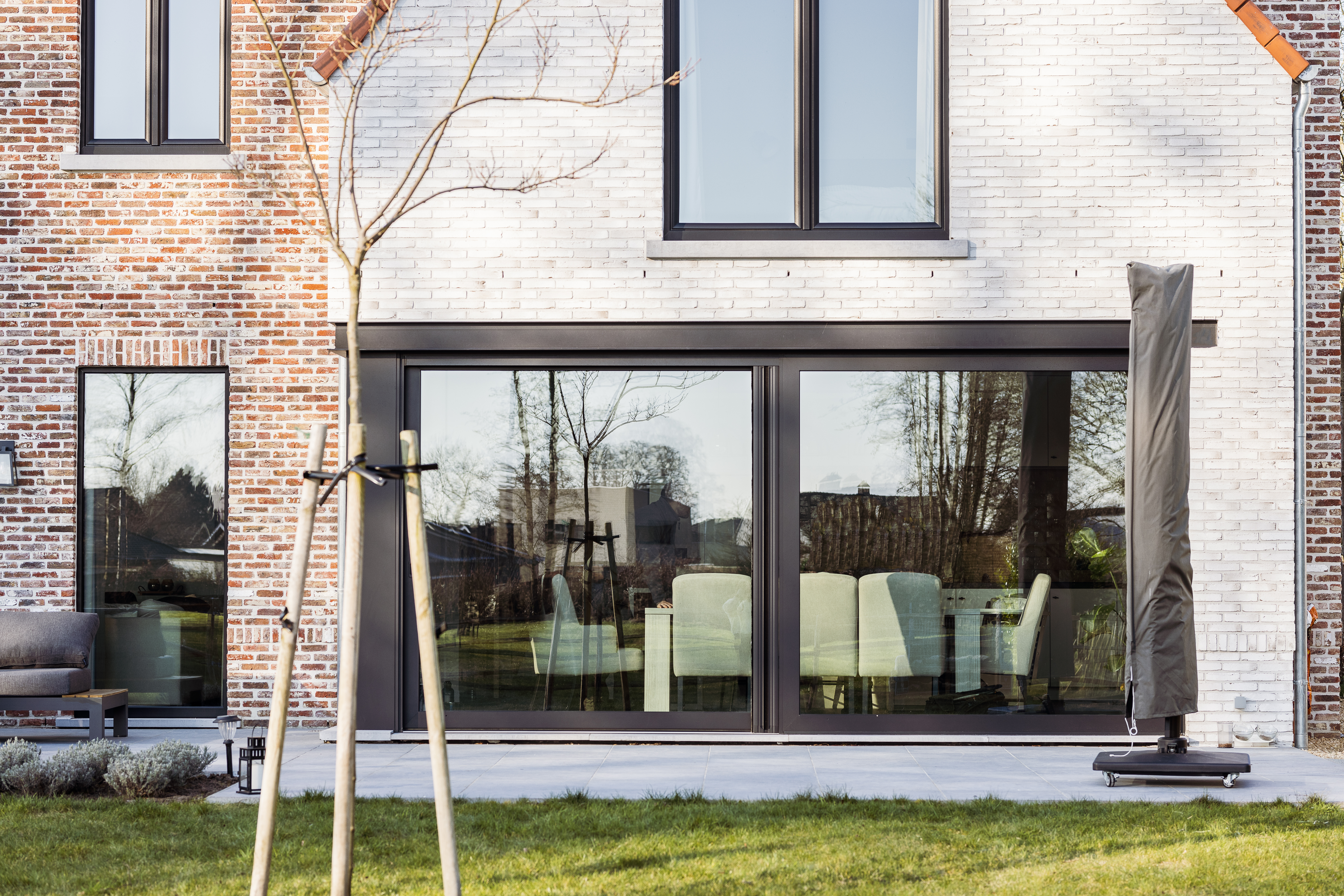 Zwart mat ALU Visoglide Duorail-schuifraam in een moderne bakstenen gevel, met grote glasvlakken en een zichtbaar interieur.
