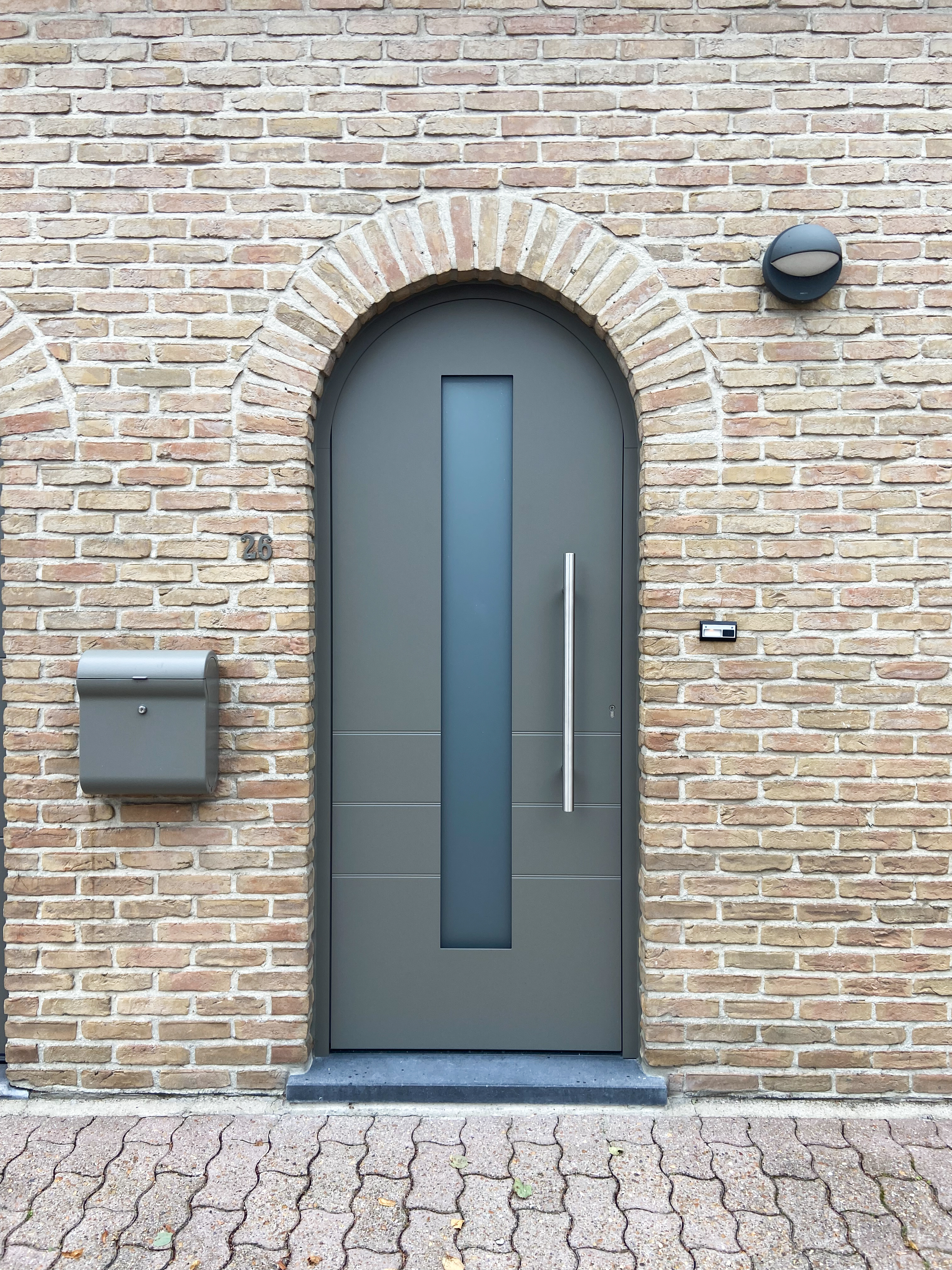 Donkere voordeur met smalle verticale inzet en lange greep in een gemetselde gevel, naast een brievenbus, passend bij een tijdloze renovatie.