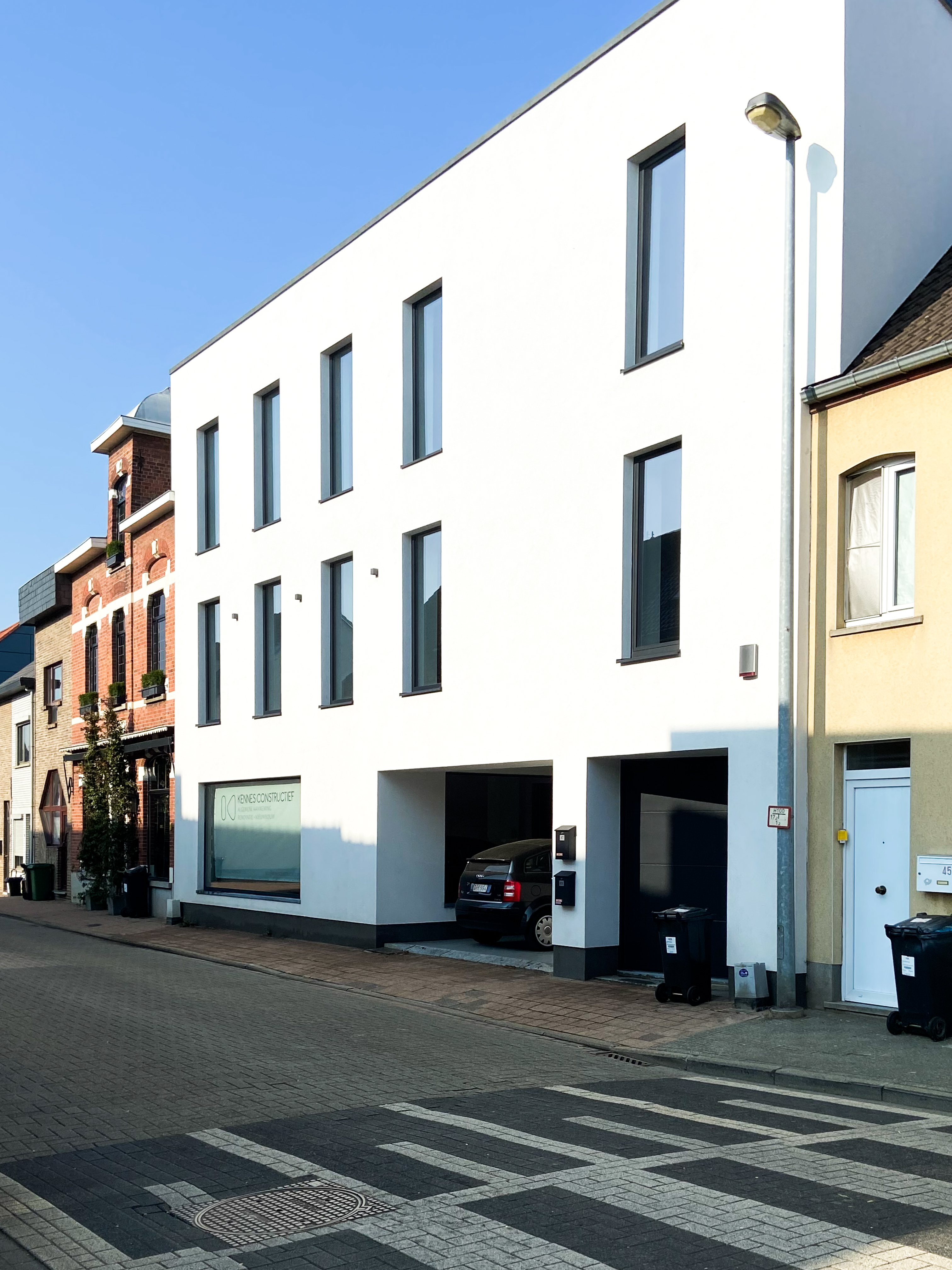 Moderne witte gevel met zwarte raamprofielen in 9005TC Zwart, een garage-inrit en inkom aan een geplaveide straat.