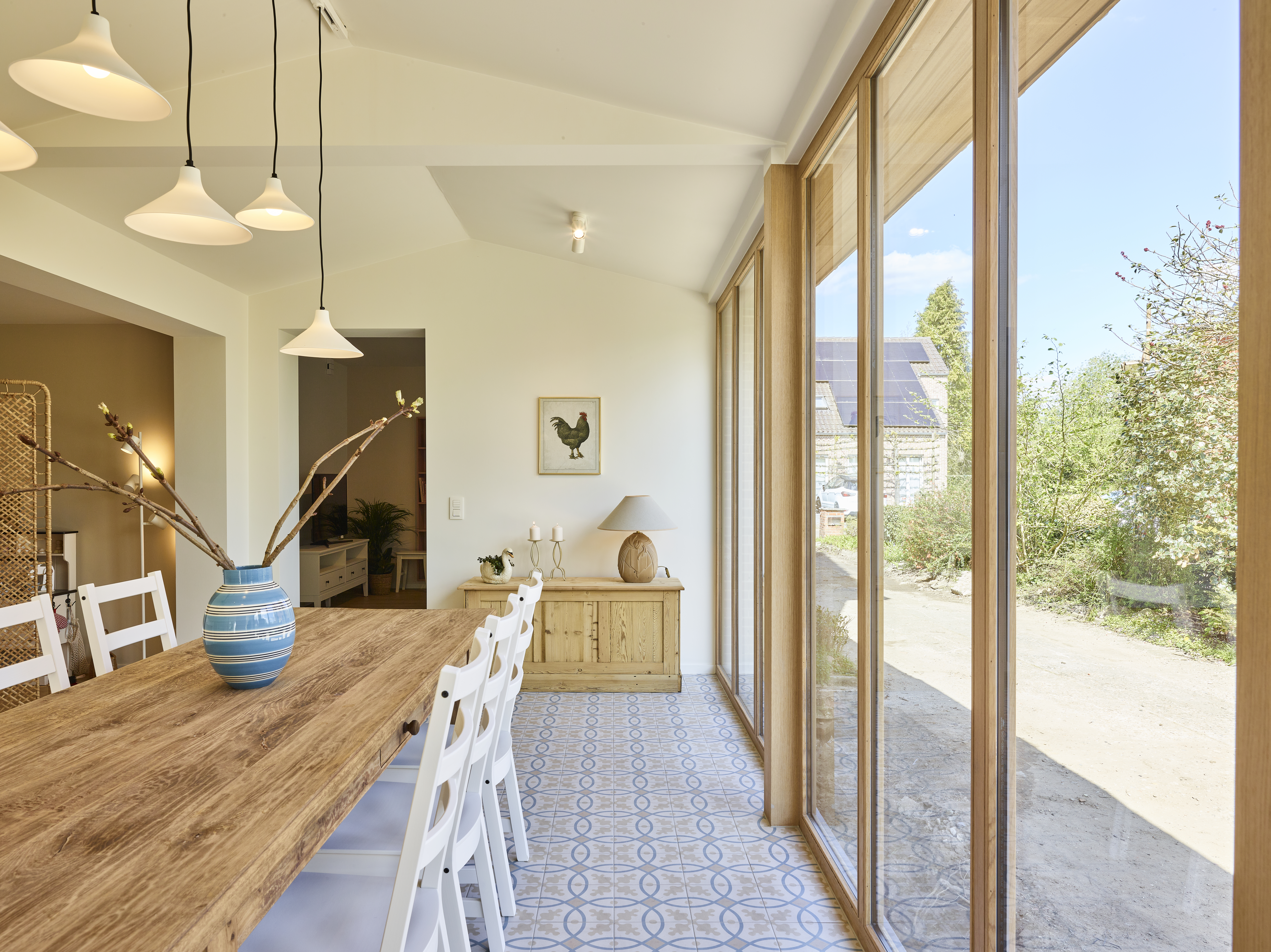 Ensemble de châssis en chêne clair laqué, avec une fenêtre triple et une partie fixe, dans un intérieur moderne près d’une table en bois.