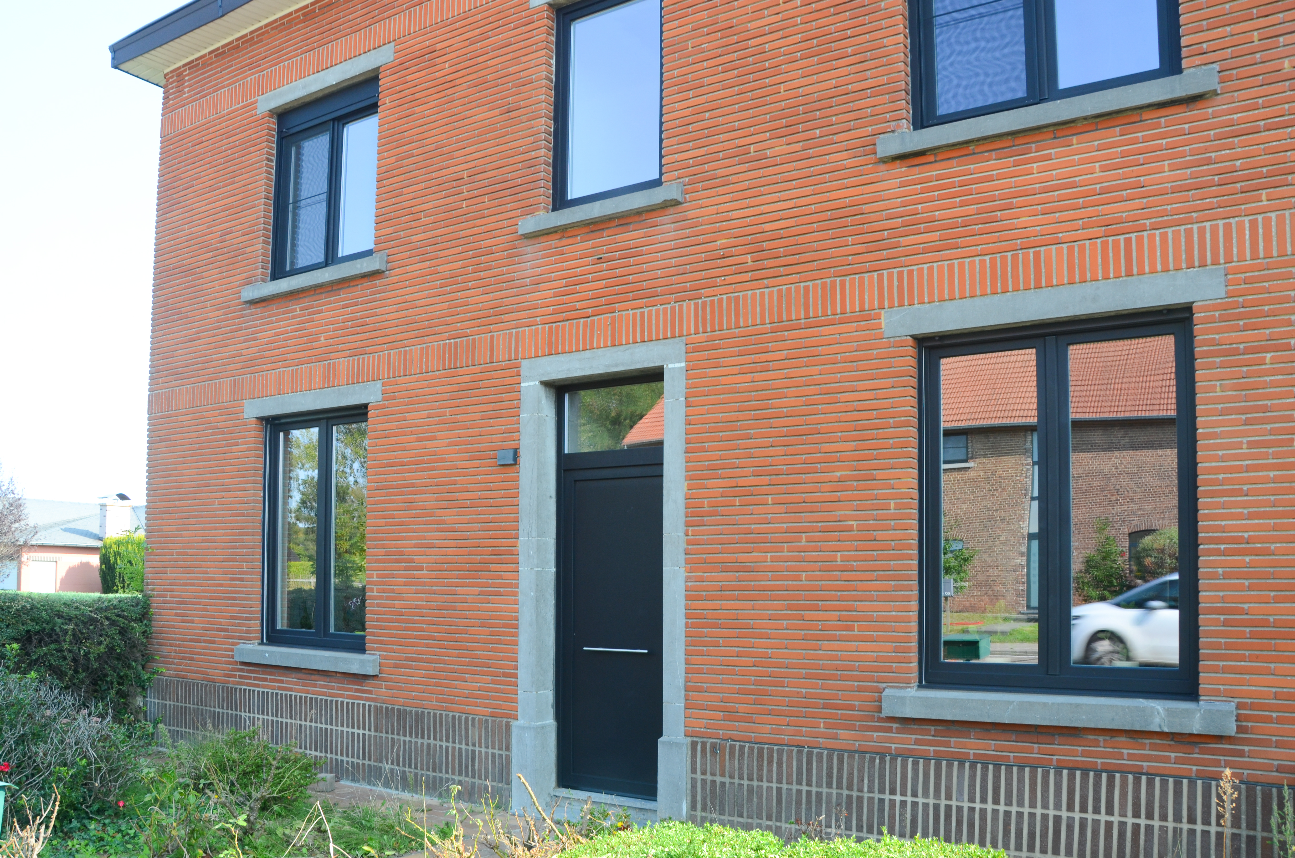 Gerenoveerde vrijstaande woning met zwarte aluminiumdeur met bovenlicht en zwarte dubbele draai-kiepramen in de bakstenen gevel.