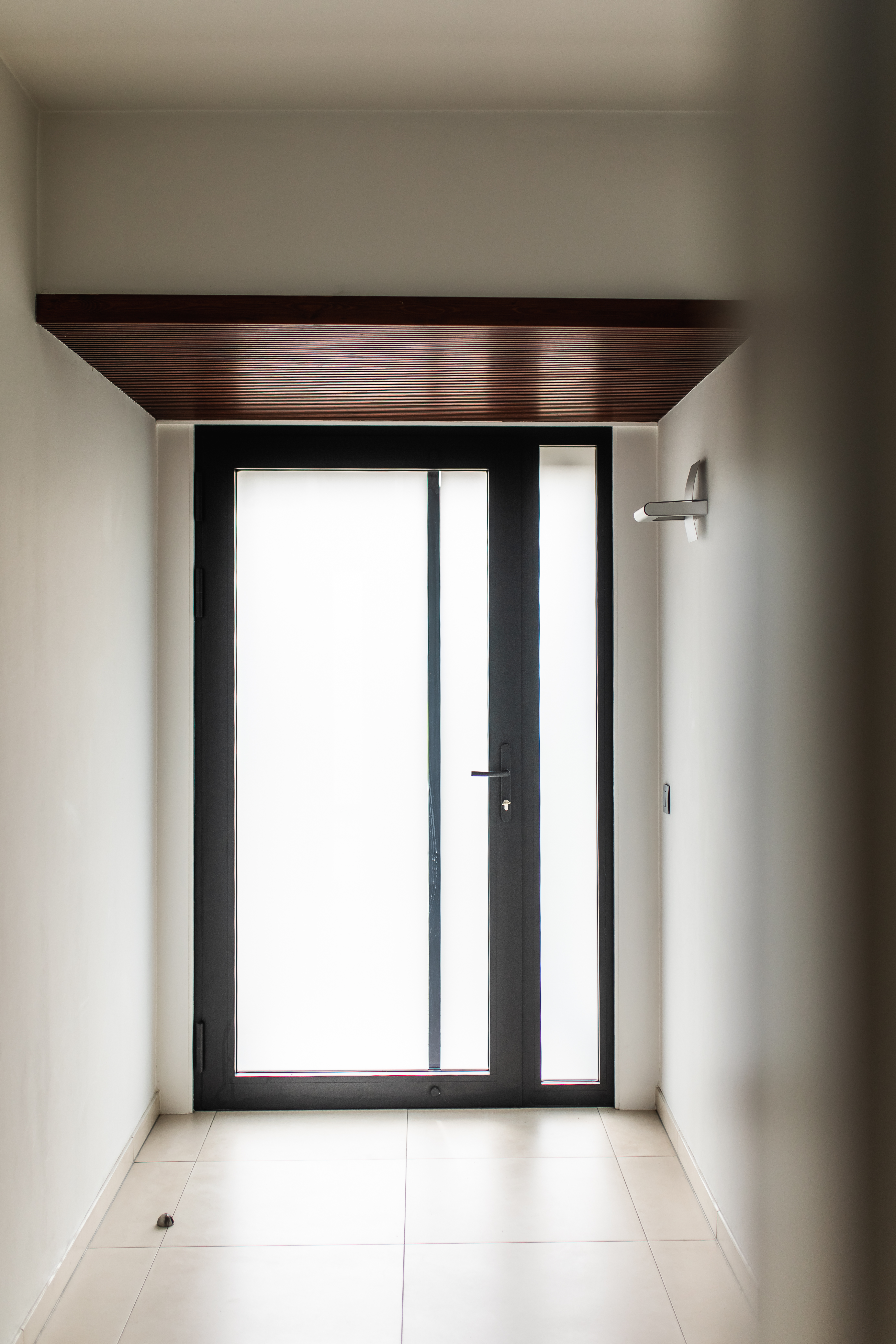 Moderne inkom met een zwarte aluminium beglaasde deur en zijlicht, geplaatst in een lichte hal.