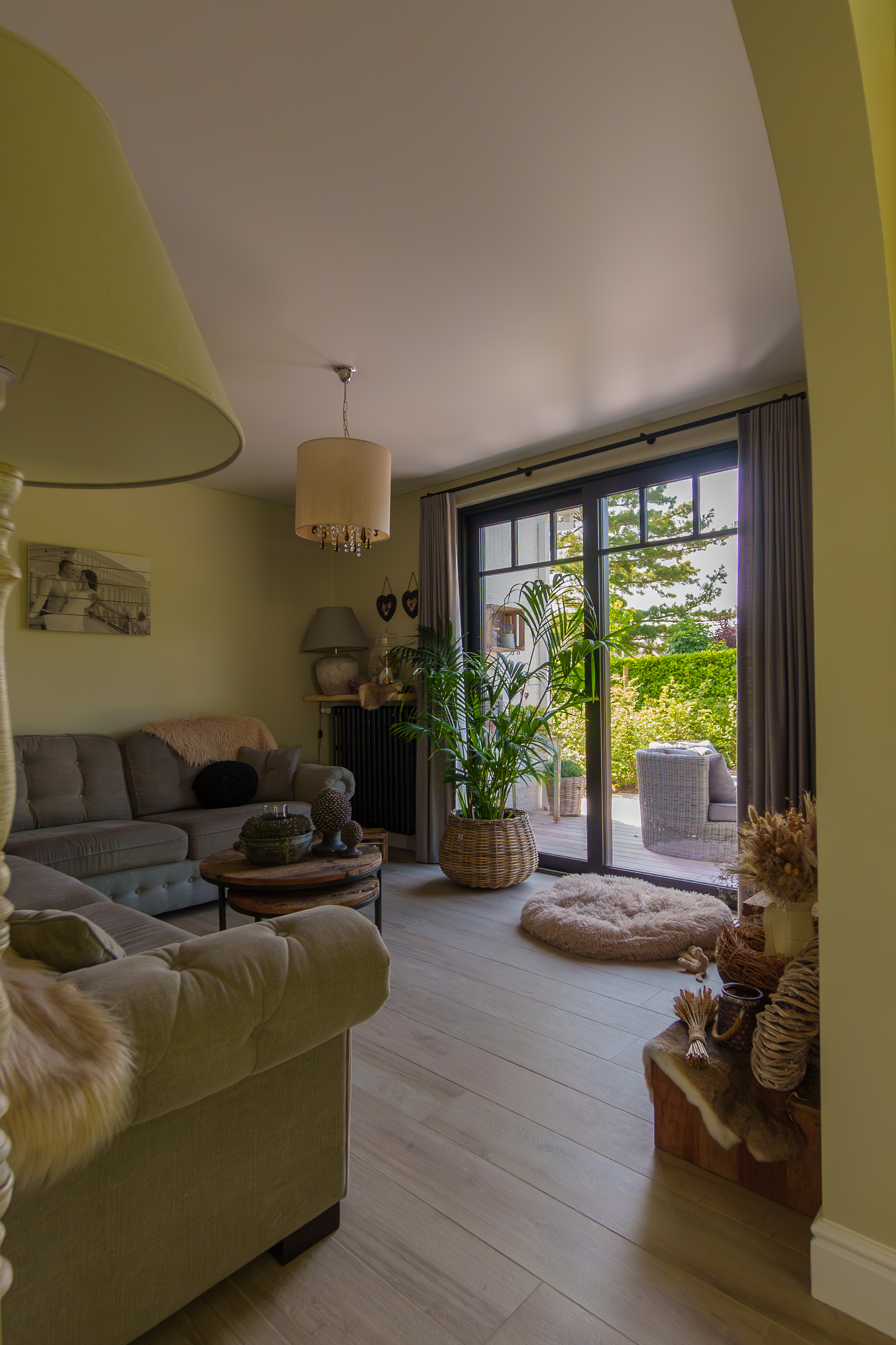 Warm ingericht landelijk woonkamer met een grote zwarte pvc-raampartij, lange gordijnen aan een duorail en veel natuurlijk licht.
