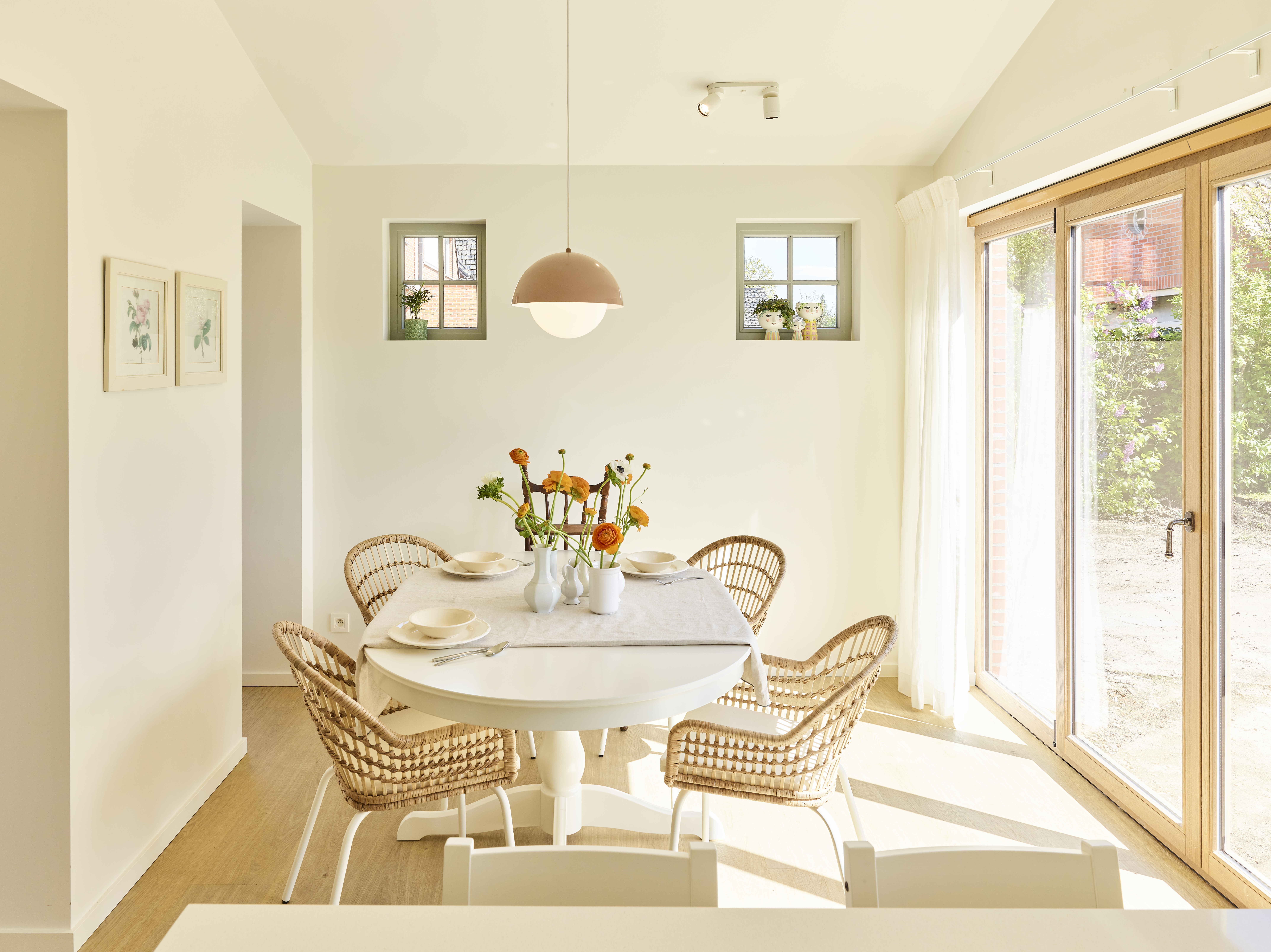 Lichte eetkamer met tafel en rieten stoelen, plus een raamgeheel in lichte eik met vierdubbel raam, draai-kipraam en vast raam in landelijke steellook.