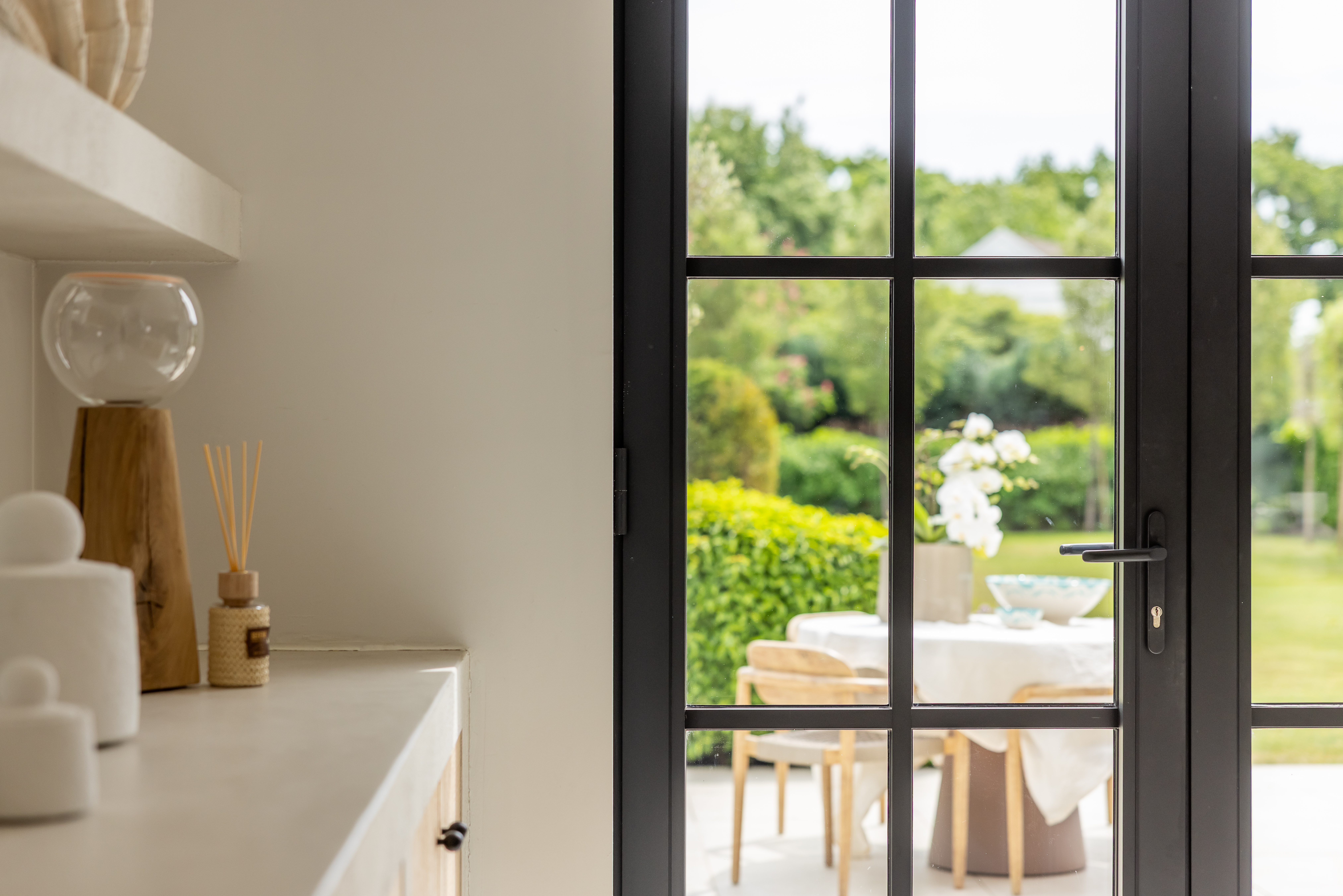 Zwarte Steel-lookdeur met fijne roedeverdeling verbindt een warm landelijk interieur met het terras en de groene tuin.