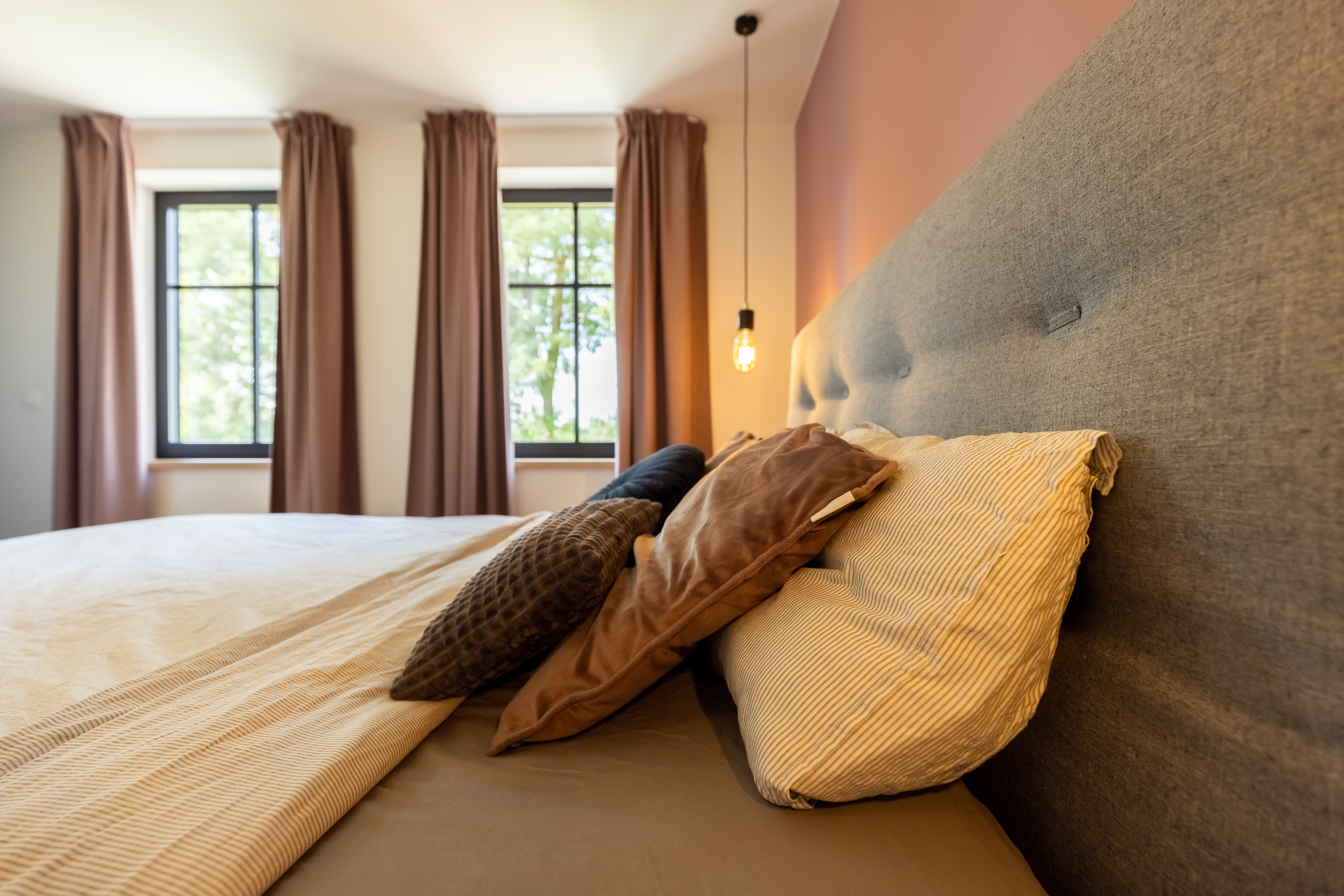 Draai-kipramen met diepzwarte raamprofielen in een warme, landelijke slaapkamer, naast een gestoffeerd bed met uitzicht op het groen.
