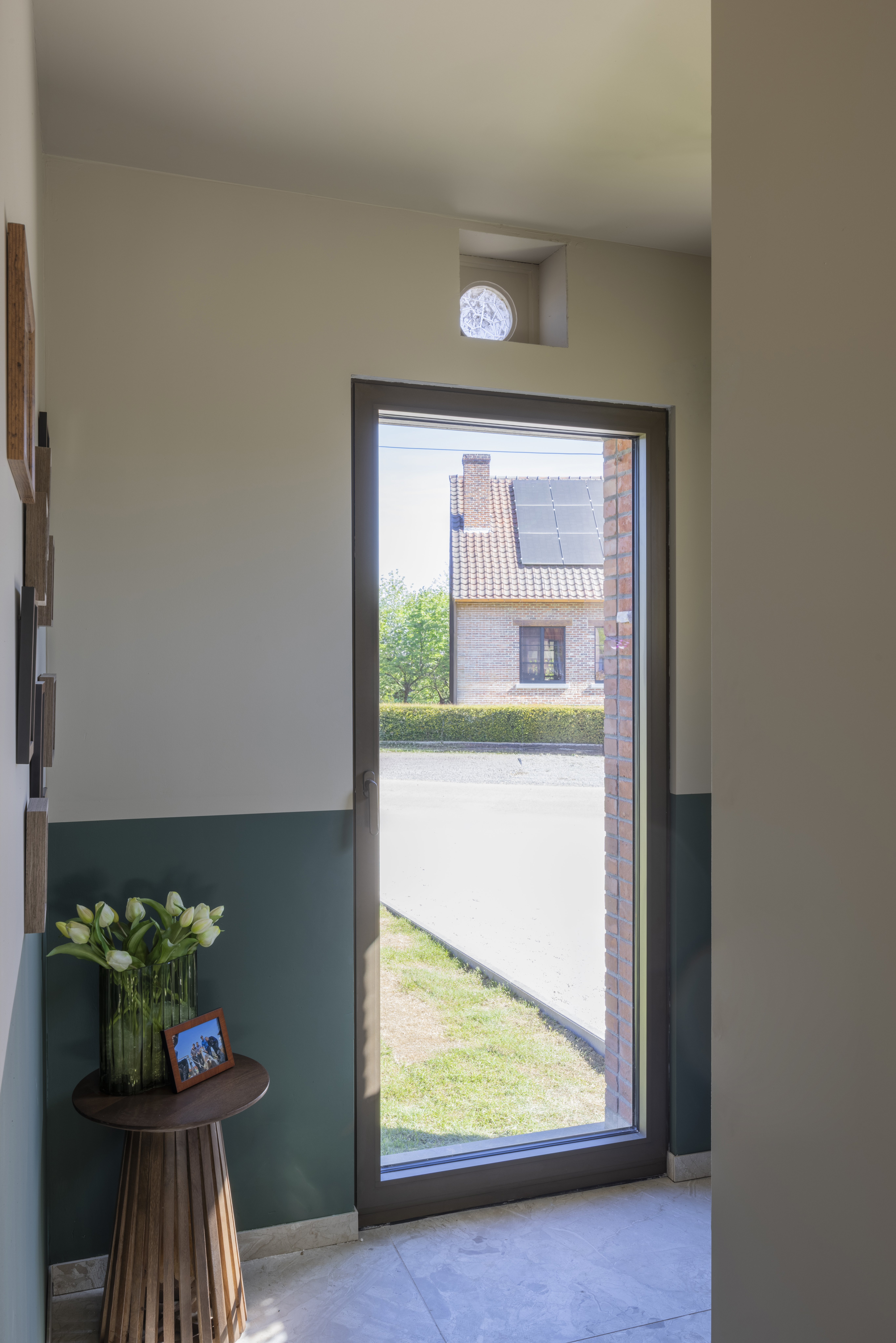 KOMFORT EVO small draai-kipraam met brons geanodiseerd raamprofiel in een lichte inkomhal, met zicht op een gevel en tuin.