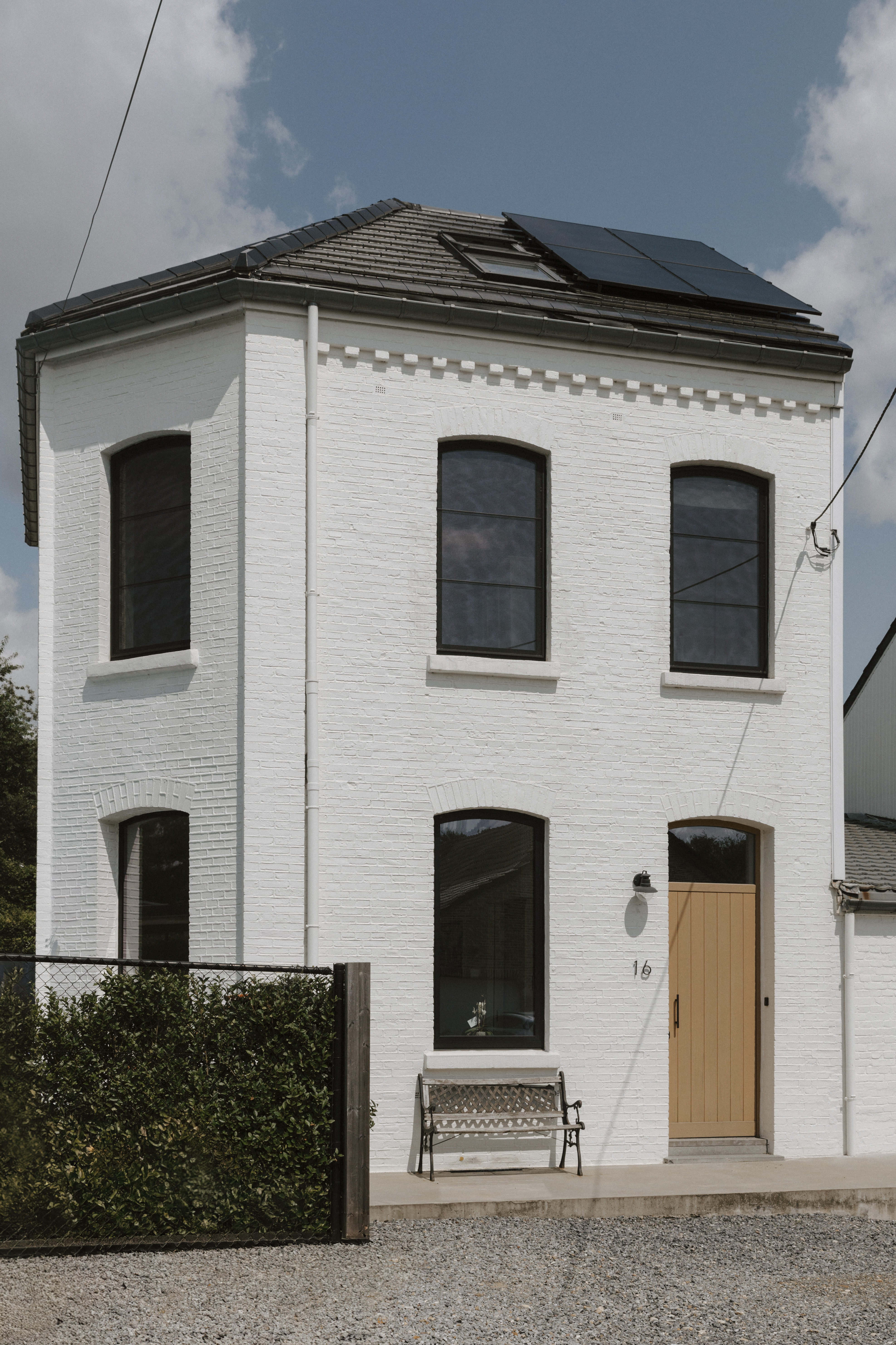 Witte bakstenen gevel met meerdere zwarte draai-kipramen, een houten deur en een dakraam in een rustige woonstraat.
