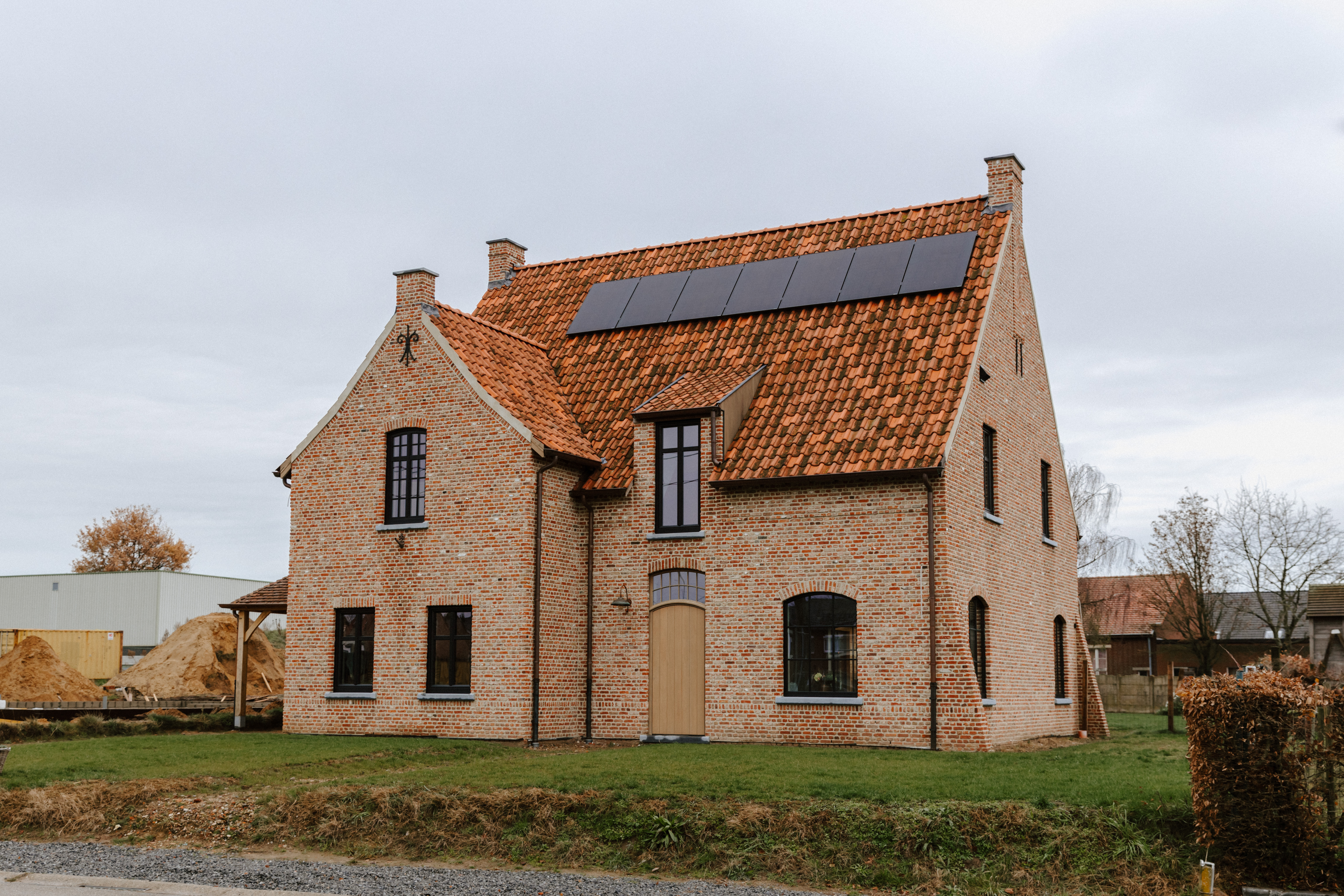 Vrijstaande landelijke bakstenen woning met matzwarte houten ramen, waaronder vaste en draai-kiepramen, en een voordeur met bovenlicht onder een pannendak.