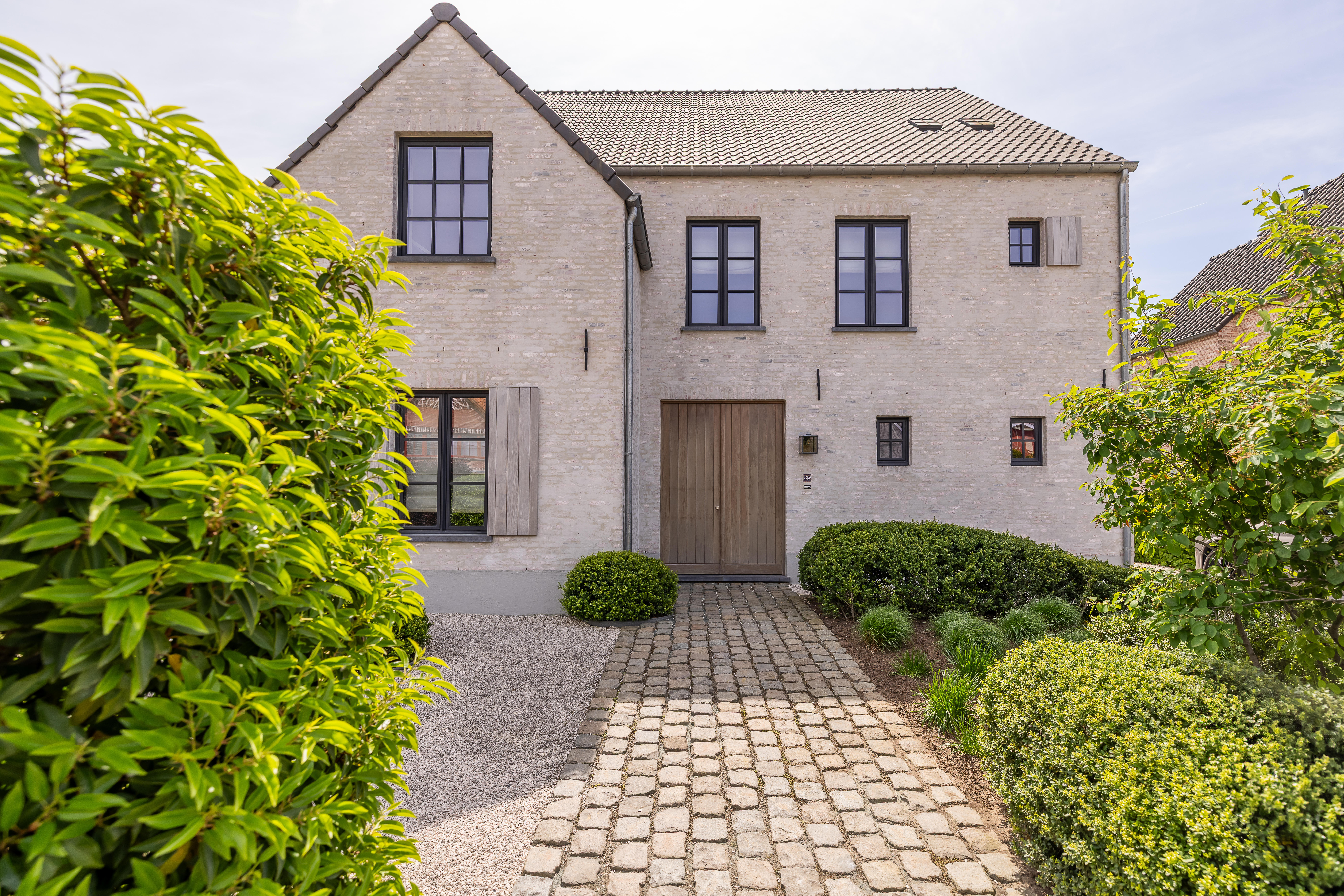 Landelijke nieuwbouwwoning met zwarte steel-lookraamprofielen, vaste ramen, dubbele ramen en draai-kipramen in een lichte bakstenen gevel.