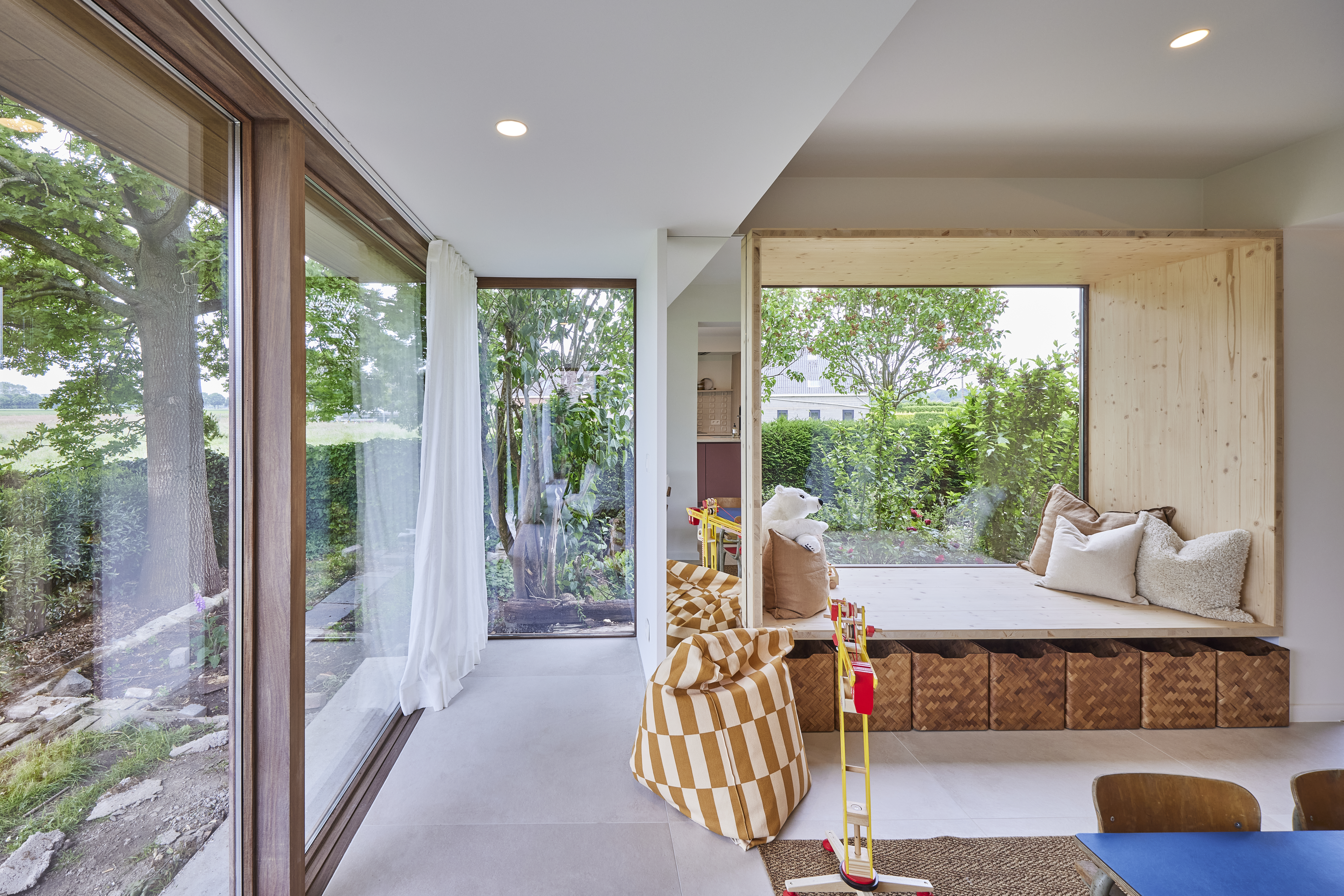 Een RE Modern vast raam met Rubio Natural-afwerking en Afromosia-houten raamprofielen in een lichte woonkamer, met zicht op de groene tuin.