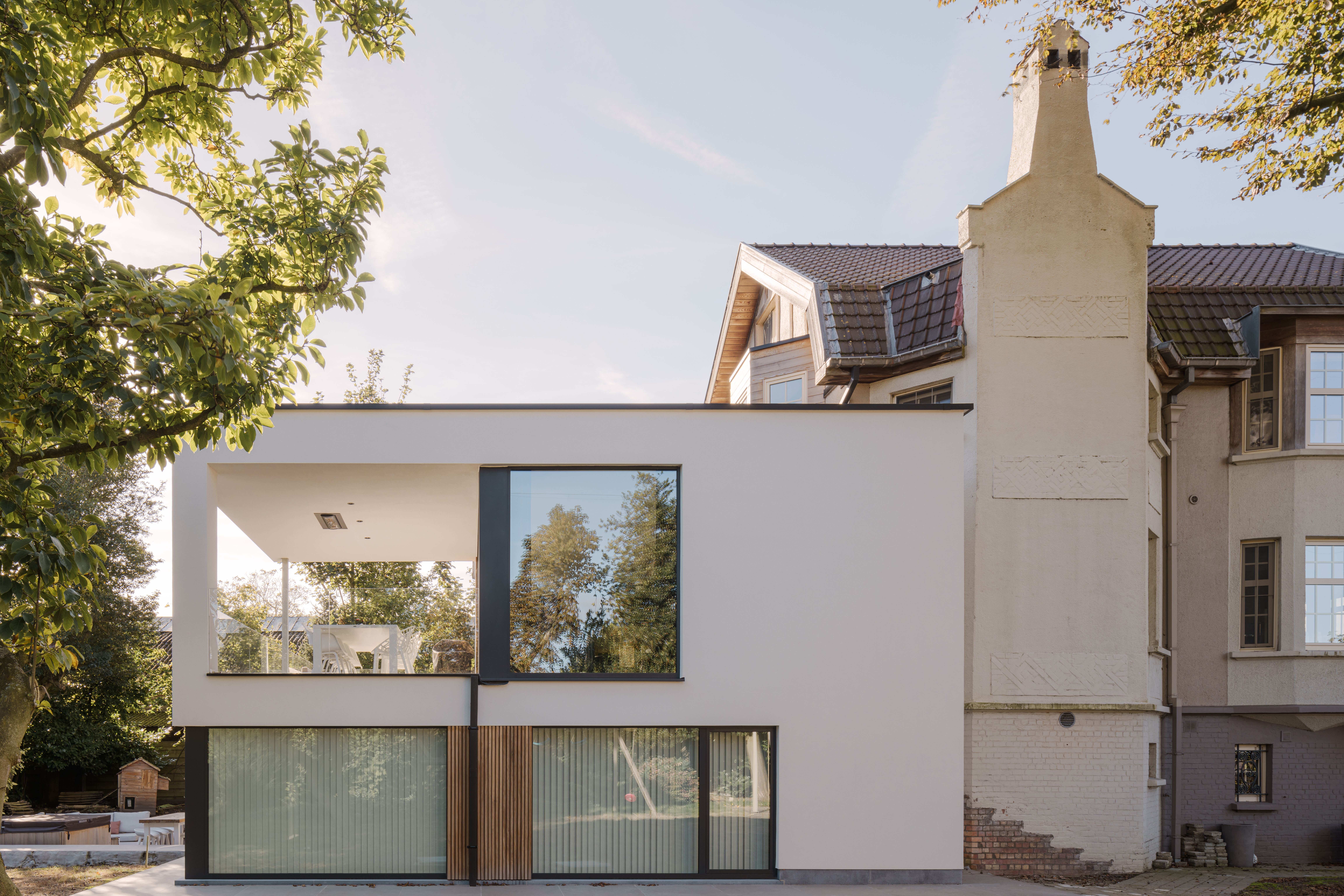 Moderne nieuwbouw met vaste ramen in zwarte raamprofielen, geïntegreerd in een witte aanbouw naast een karaktervolle bestaande woning.