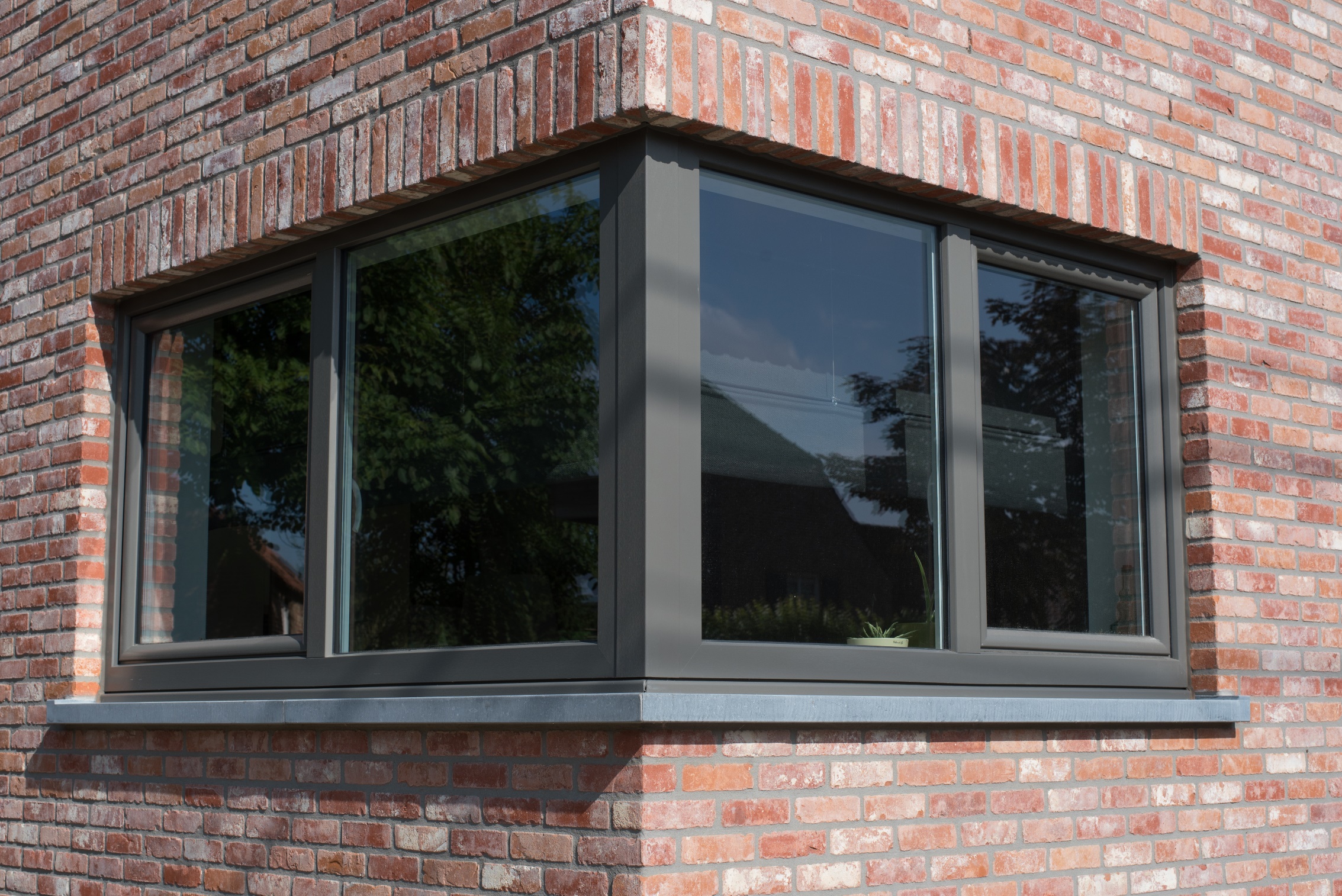 Kwartsgrijze NERF-raamprofielen vormen een hoekopstelling in de warme bakstenen gevel van een tijdloze nieuwbouwwoning.