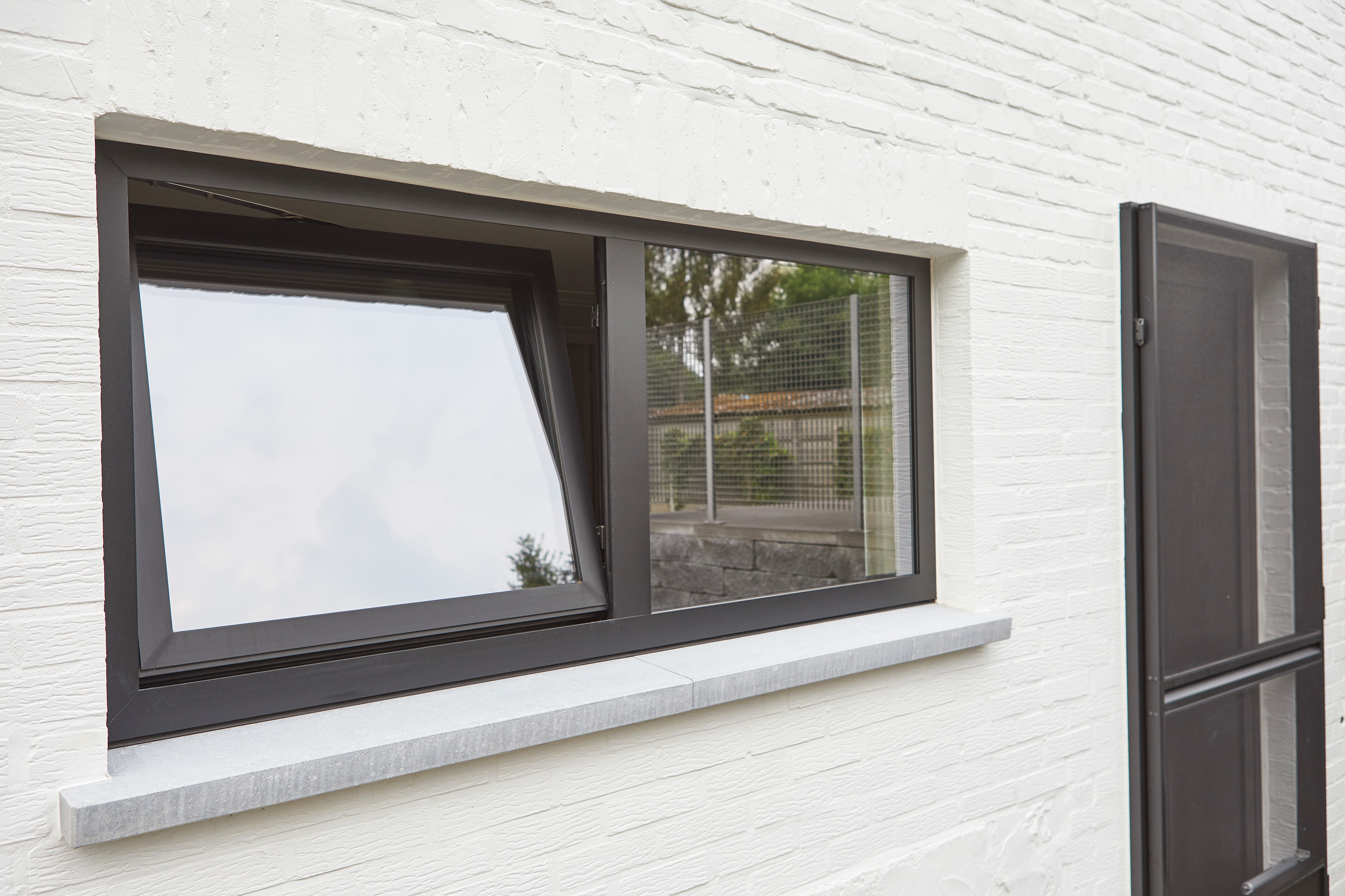 Moderne witte bakstenen gevel met zwart steellookraam en bijpassende deur, strak vormgegeven en passend bij een gerenoveerde woning.