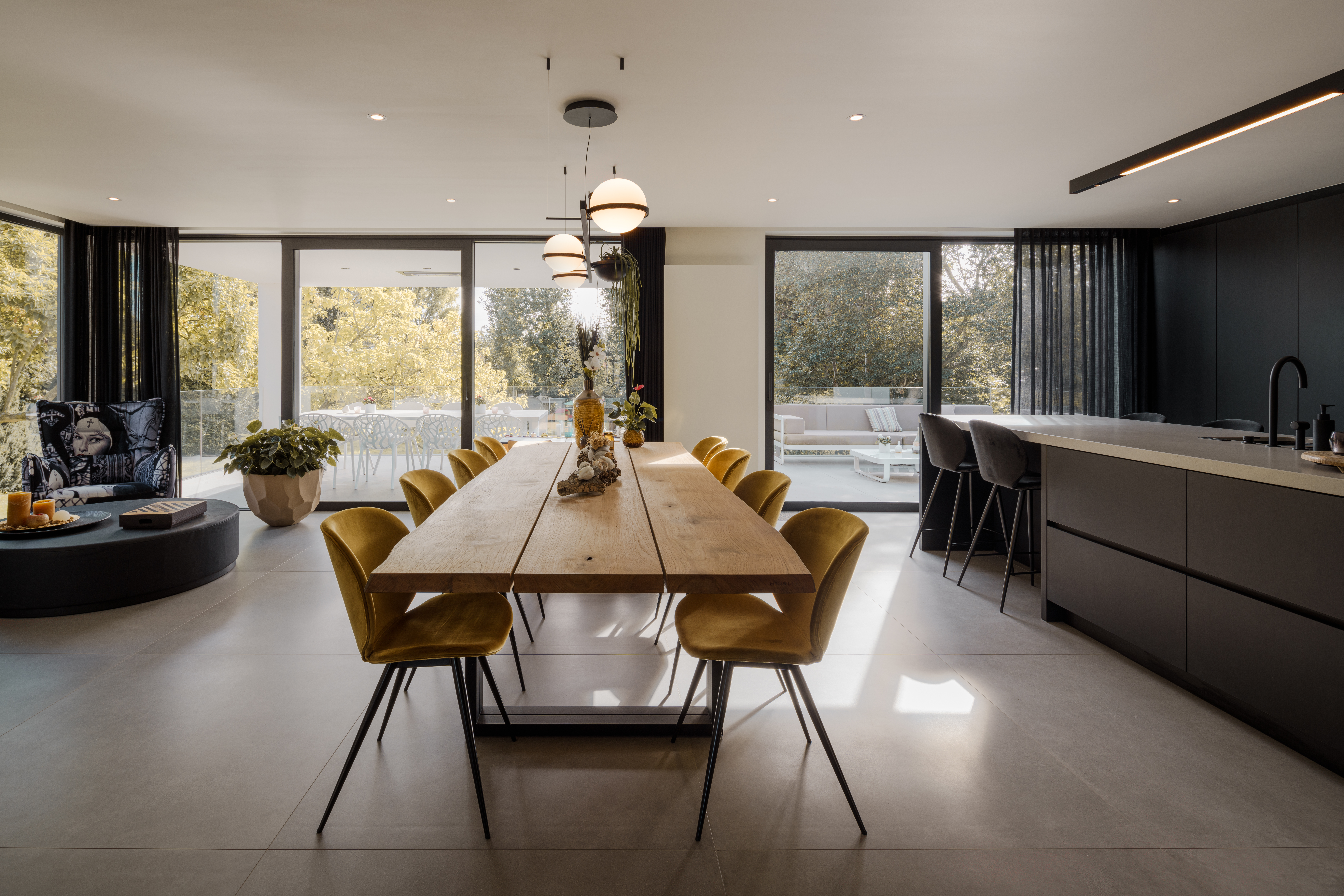 Modern eetgedeelte met zwart ALU Visoglide Monorail-schuifraam, ruime beglazing, houten tafel en donker kookeiland in een nieuwbouwwoning.