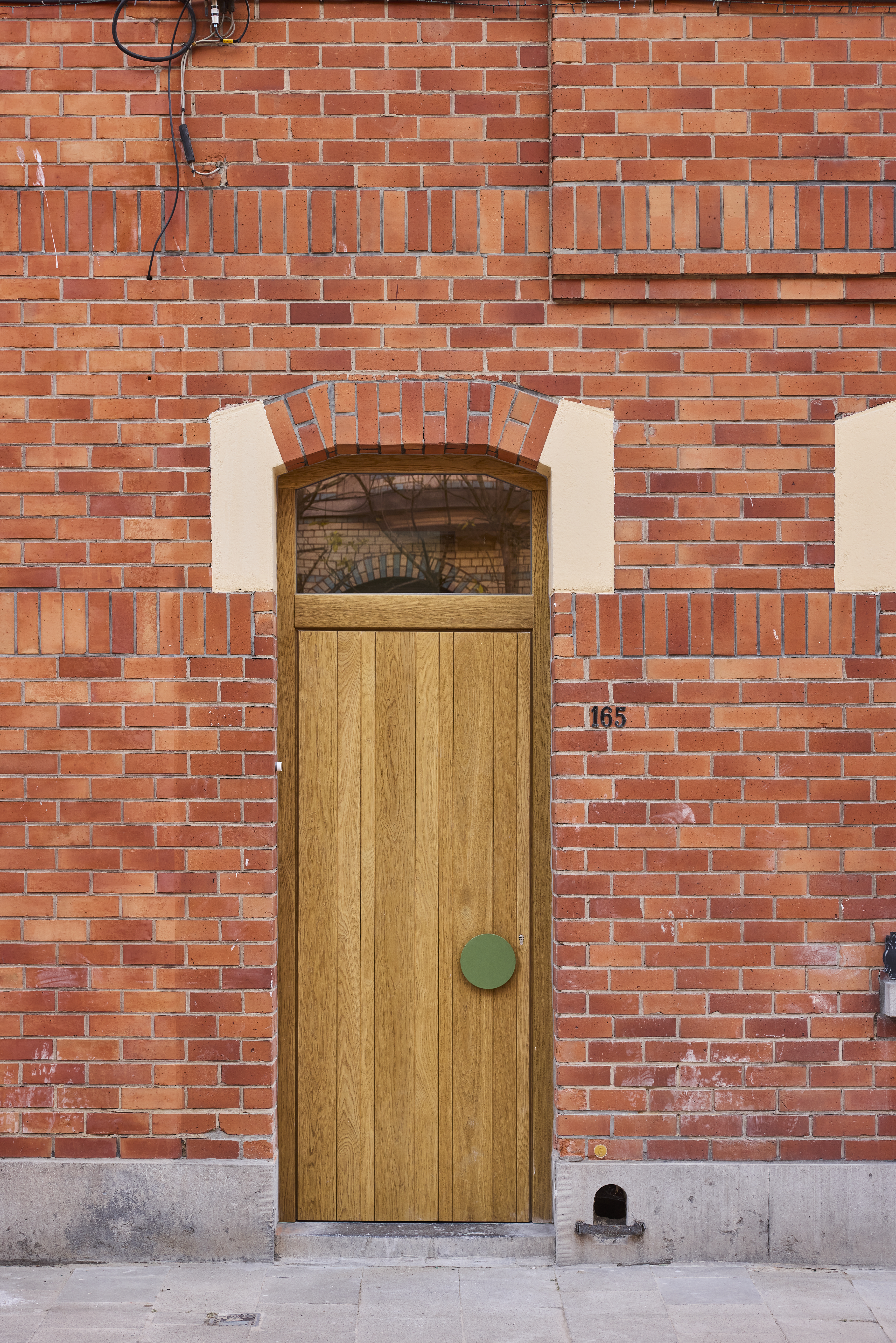 Porte en chêne avec imposte vitrée dans une façade en briques rouges, avec soubassement en pierre naturelle et poignée verte.