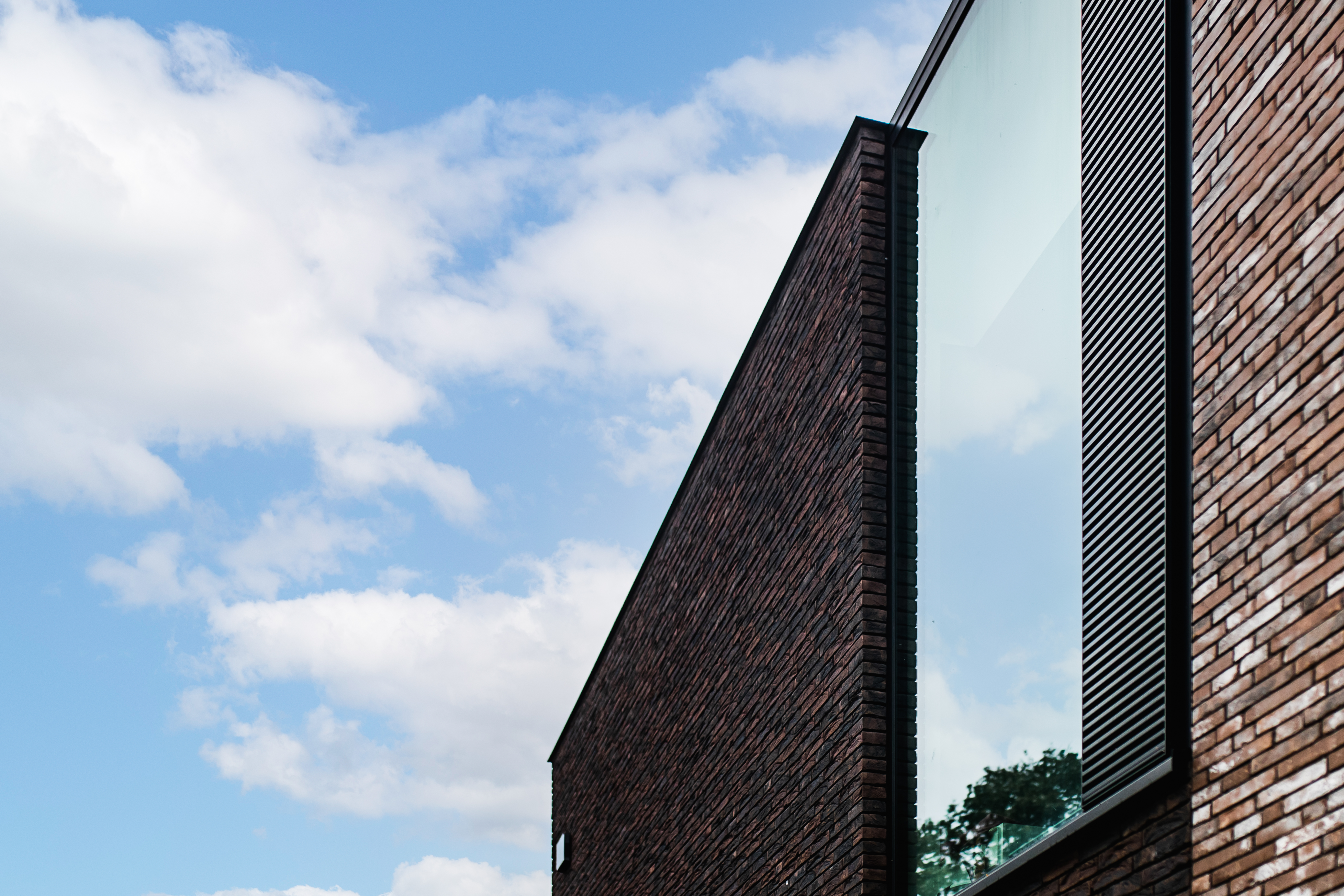 Moderne bakstenen gevel van een nieuwbouwwoning met een groot donker raam en karaktervolle architectuur van een open bebouwing onder een blauwe hemel.