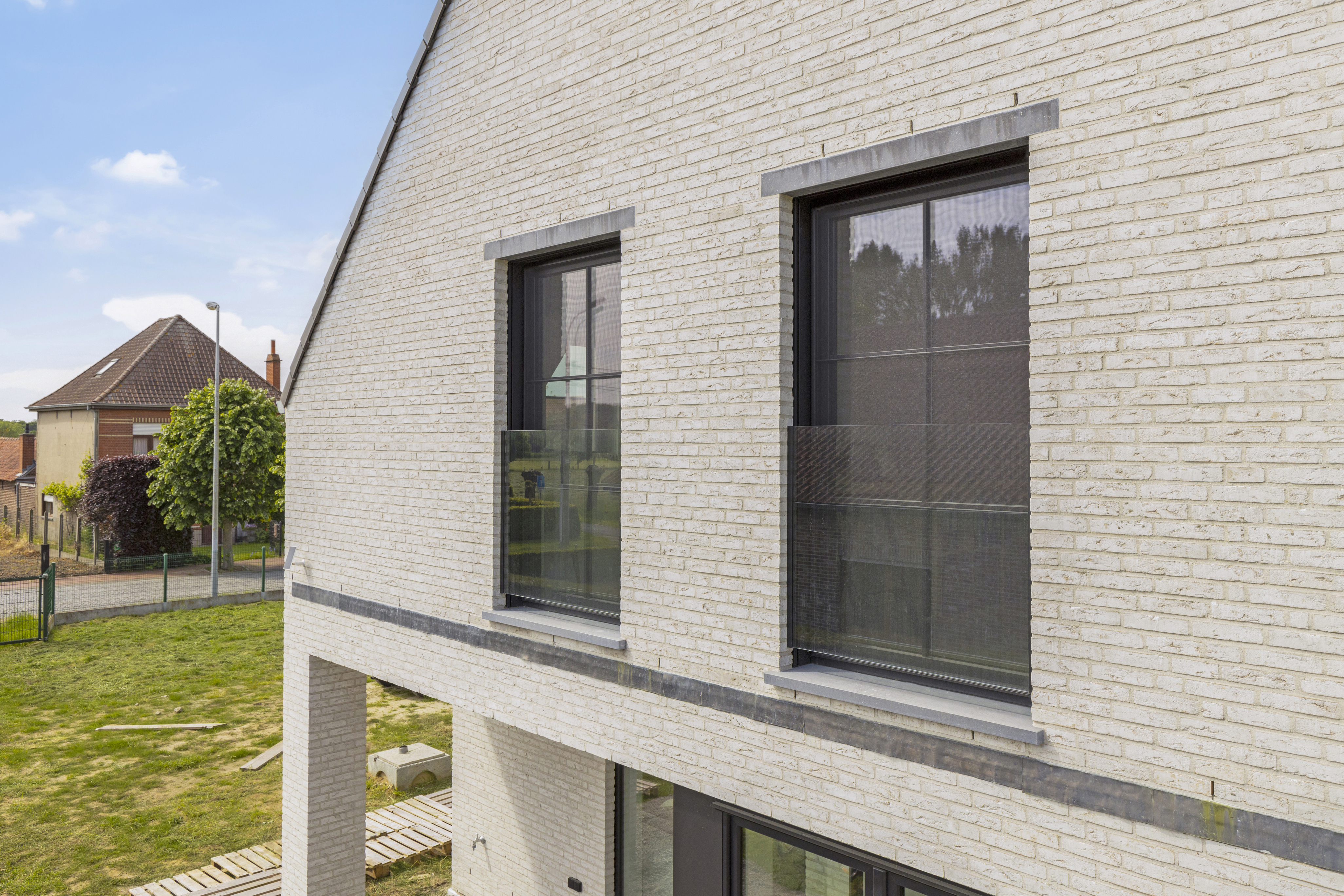 Twee matzwarte draai-kipramen met vliegenramen in de lichte bakstenen gevel van een moderne vrijstaande woning in een landelijke omgeving.