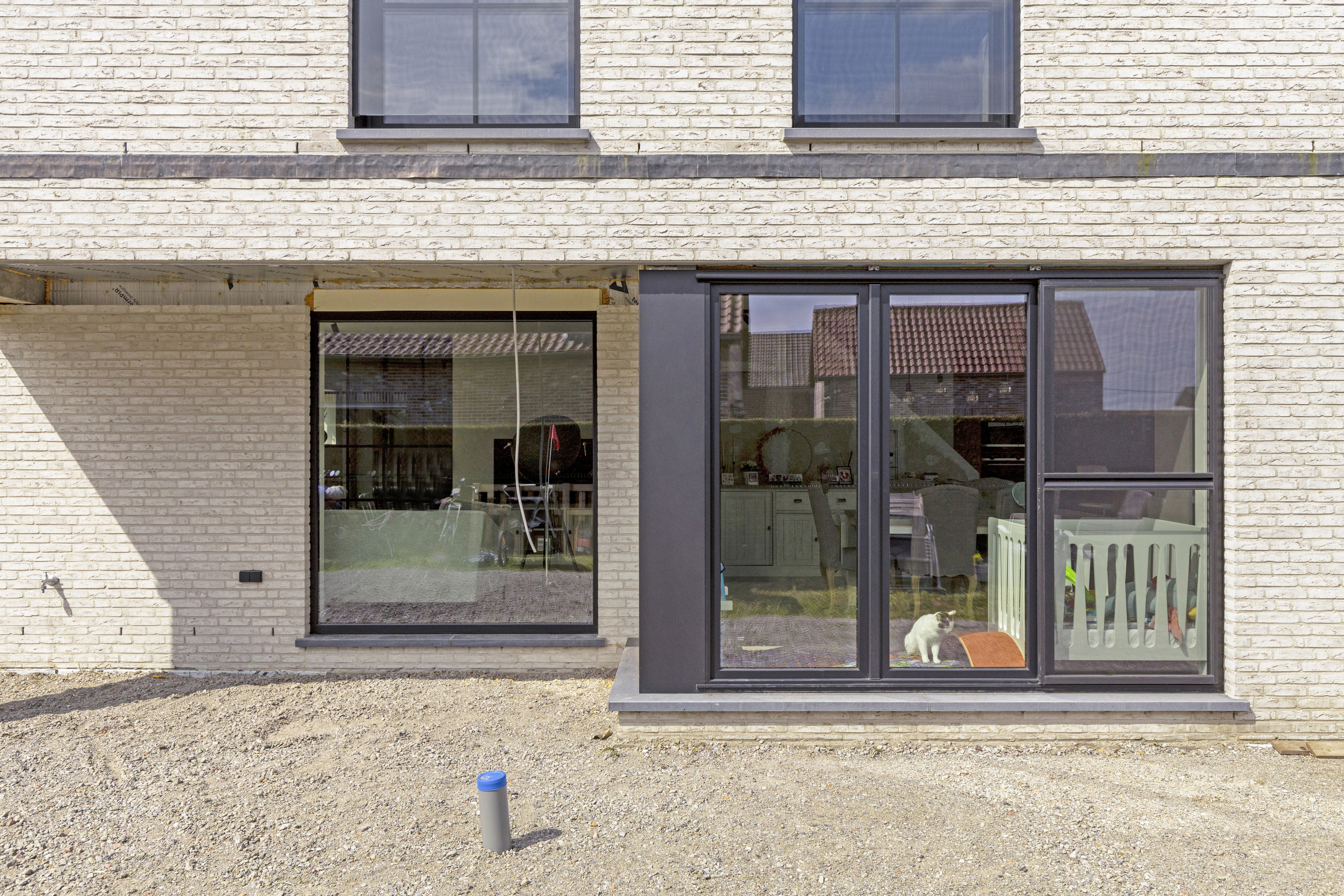 Matzwart raam met drie verticale delen en een vast raam in een lichte bakstenen gevel van een nieuwbouwwoning, met schuifvliegenraam.