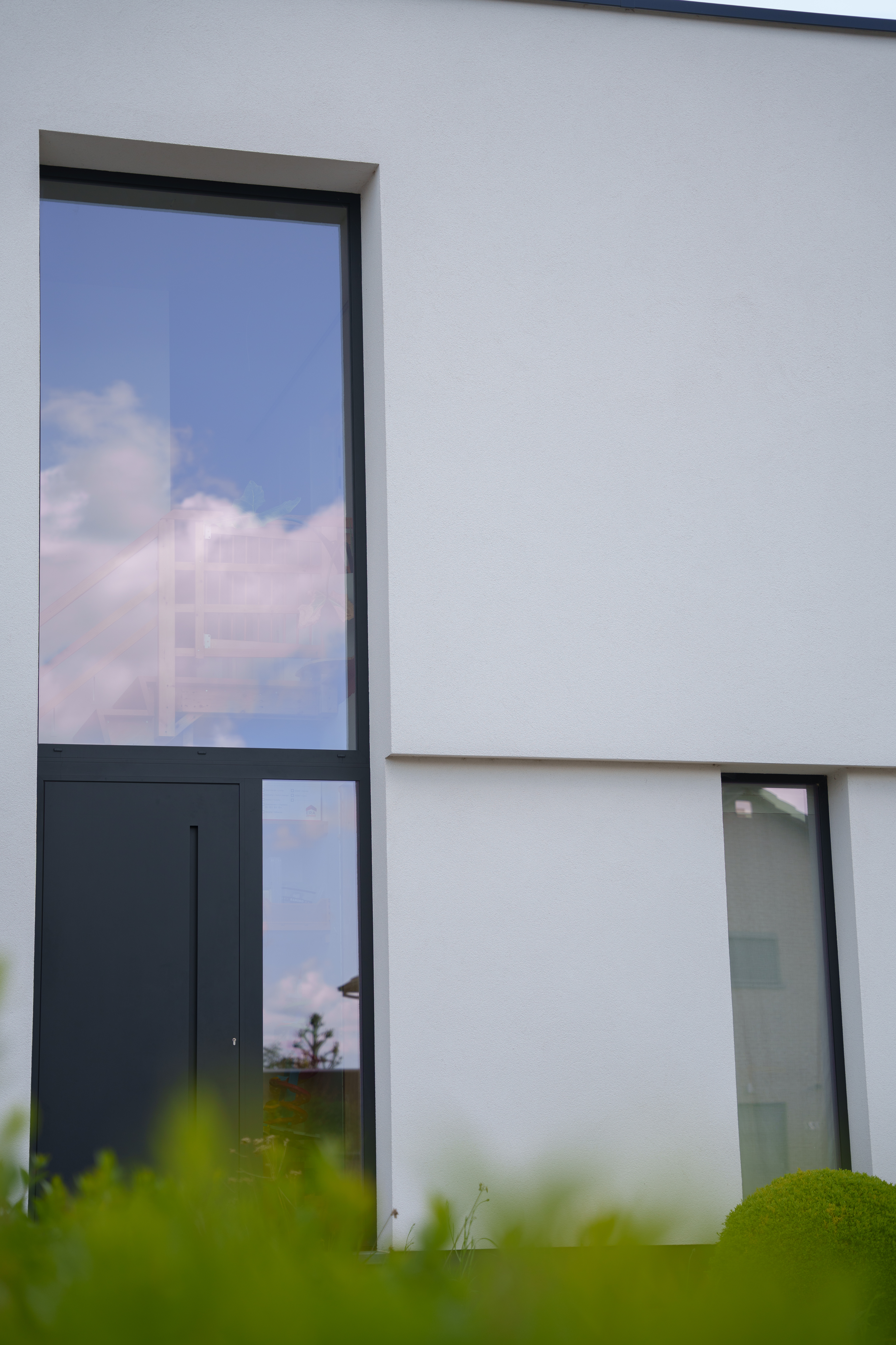 Moderne nieuwbouwgevel met vast raam in diepzwarte aluminiumprofielen, gecombineerd met een deur met zijlicht en bovenlicht.