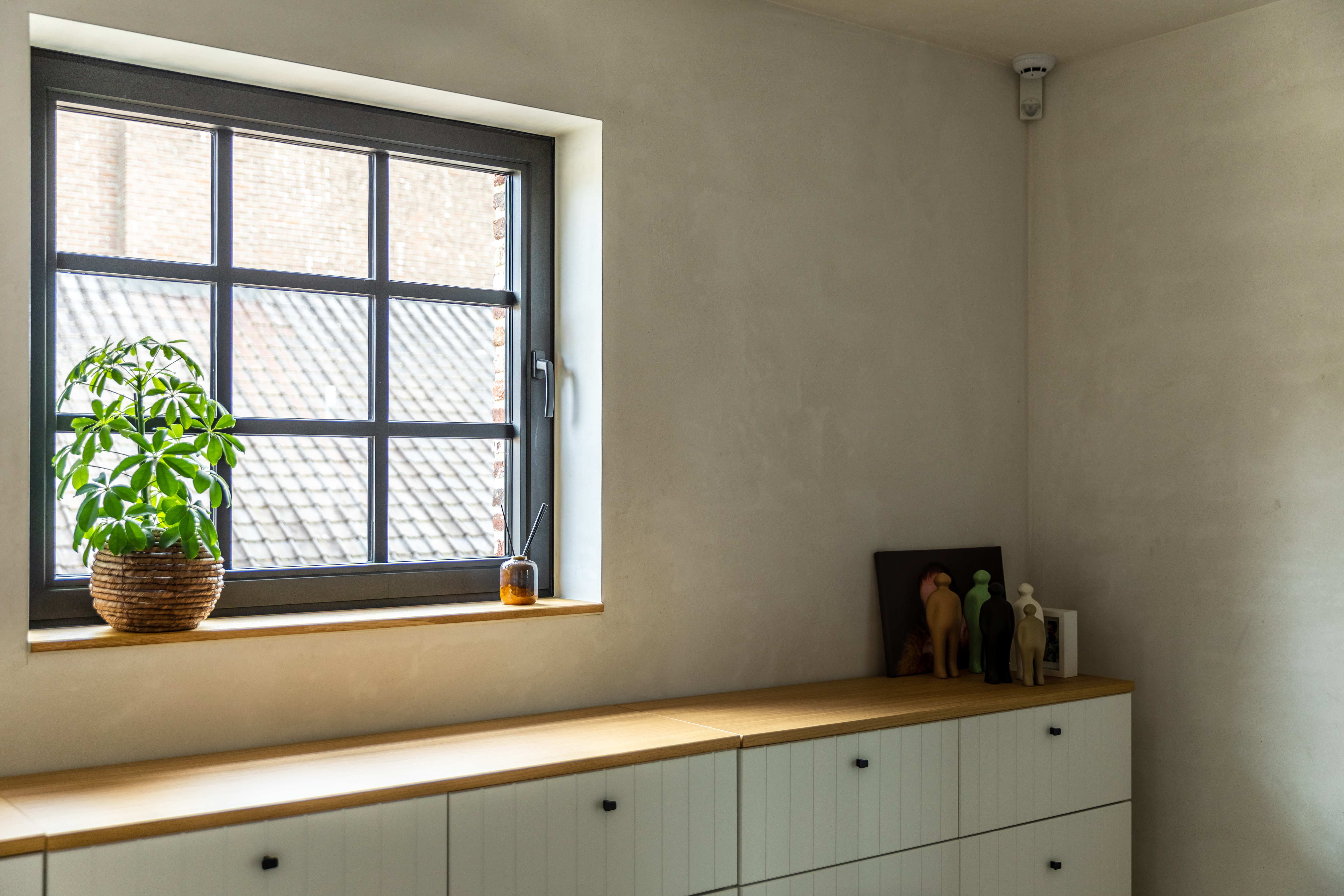 Zwart draai-kipraam in een warm, landelijk nieuwbouwinterieur, met een plant en een houten lage kast tegen een lichte wand.